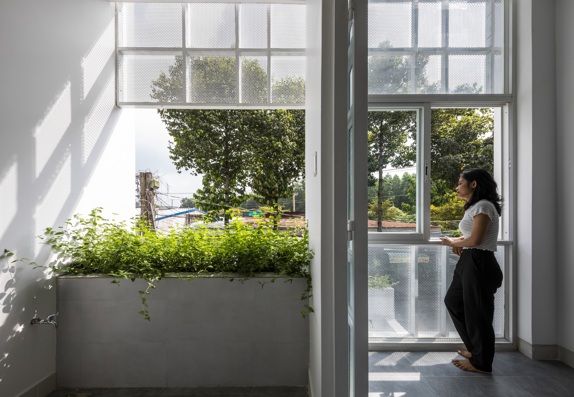 White interior balcony with planted concrete planter and a woman looking out through full-height glazed doors