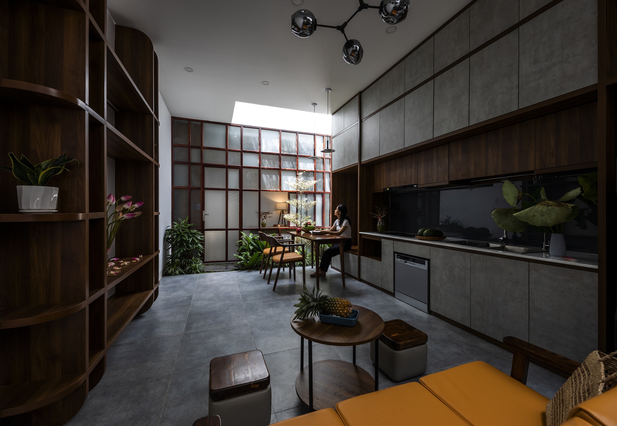 Open kitchen and dining space with dark timber cabinetry, concrete panels, and translucent gridded screen wall