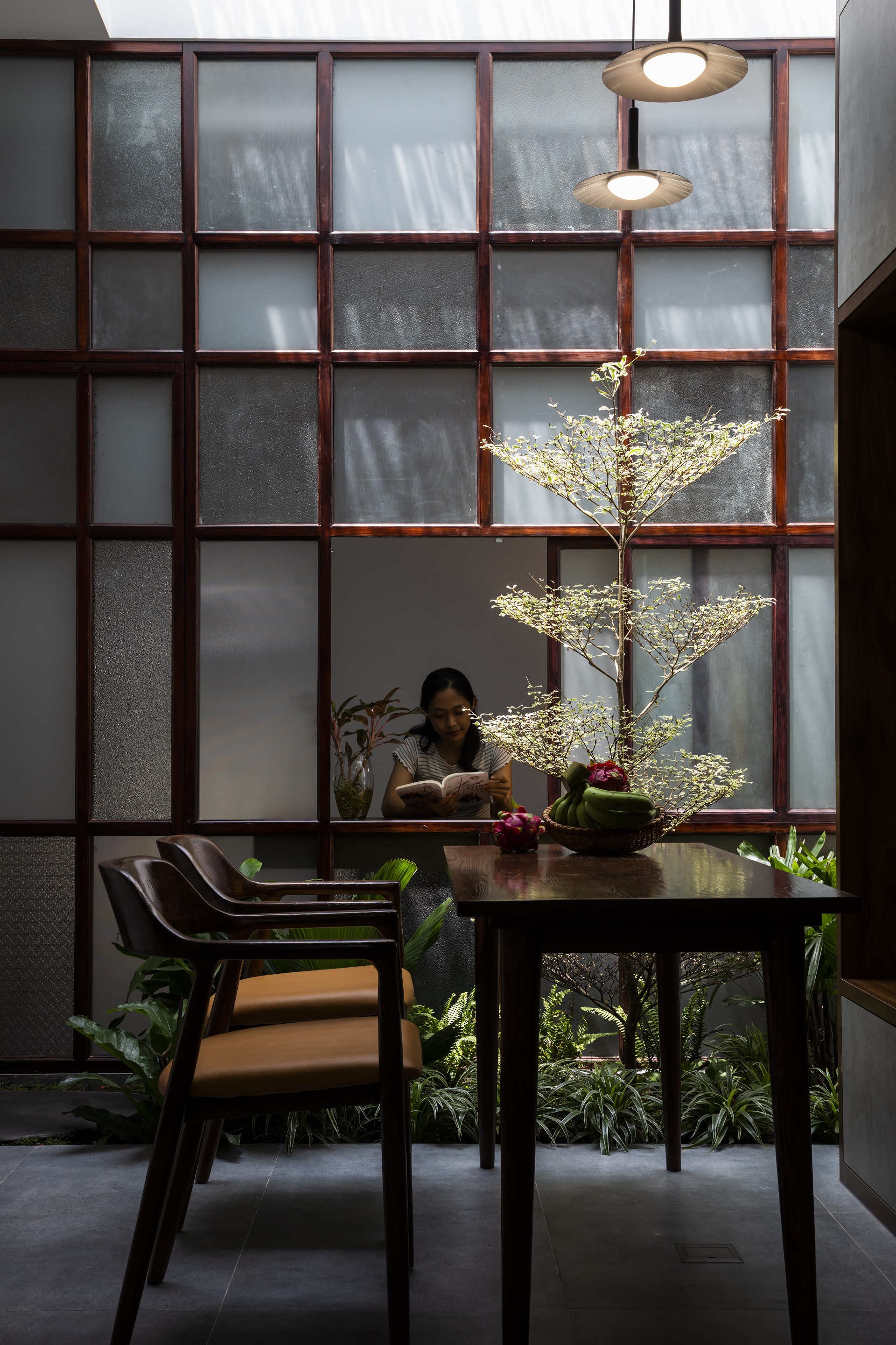 Woman reading at the dining table with a small tree and translucent screen wall behind her