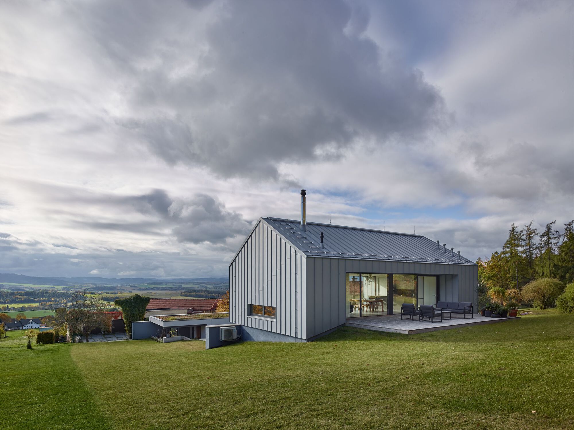 Vertical metal-clad gable volume rising from a sloped lawn under heavy autumn clouds