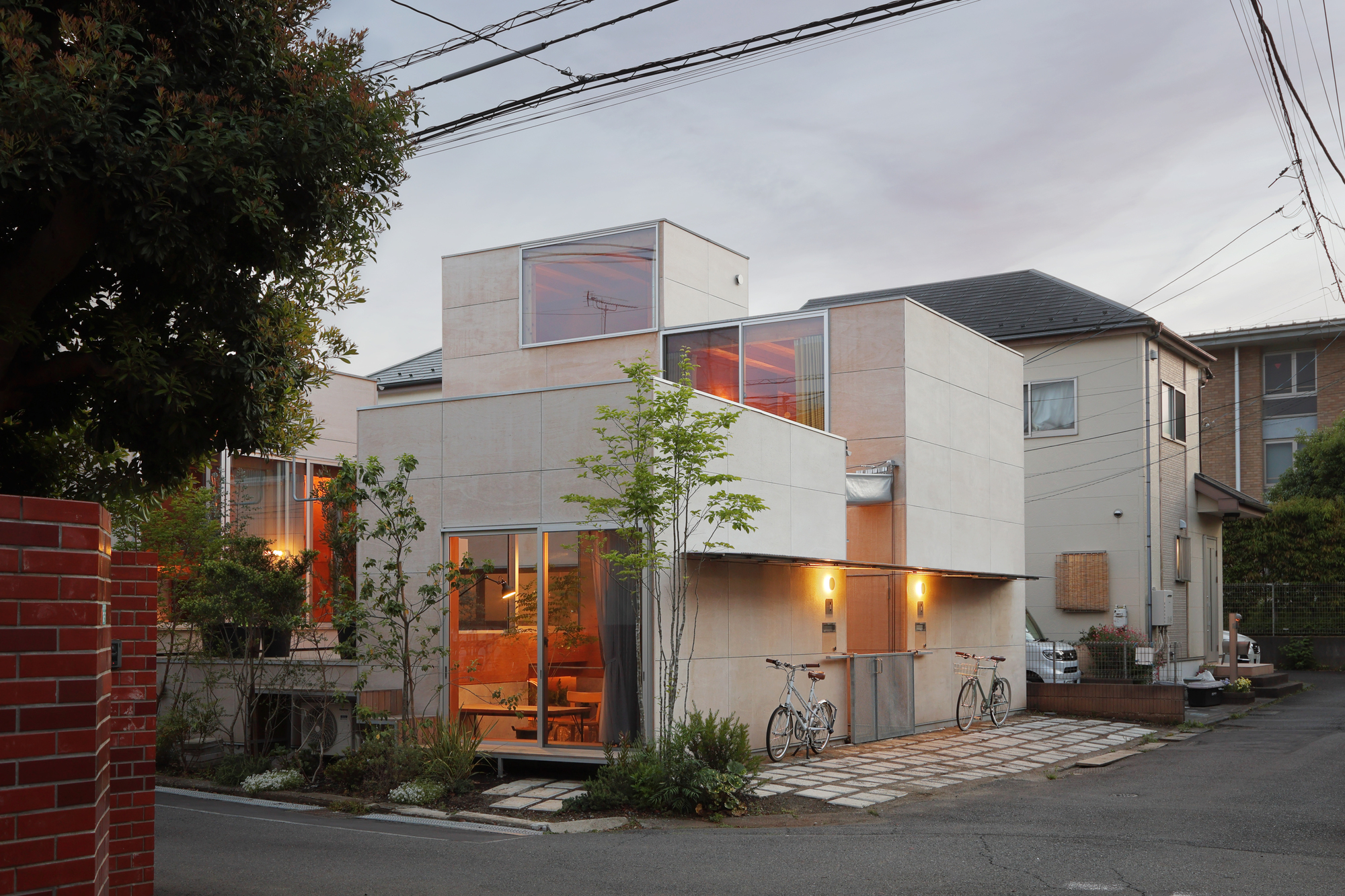 Clustered volumes with illuminated interiors and bicycles parked along the entry at dusk