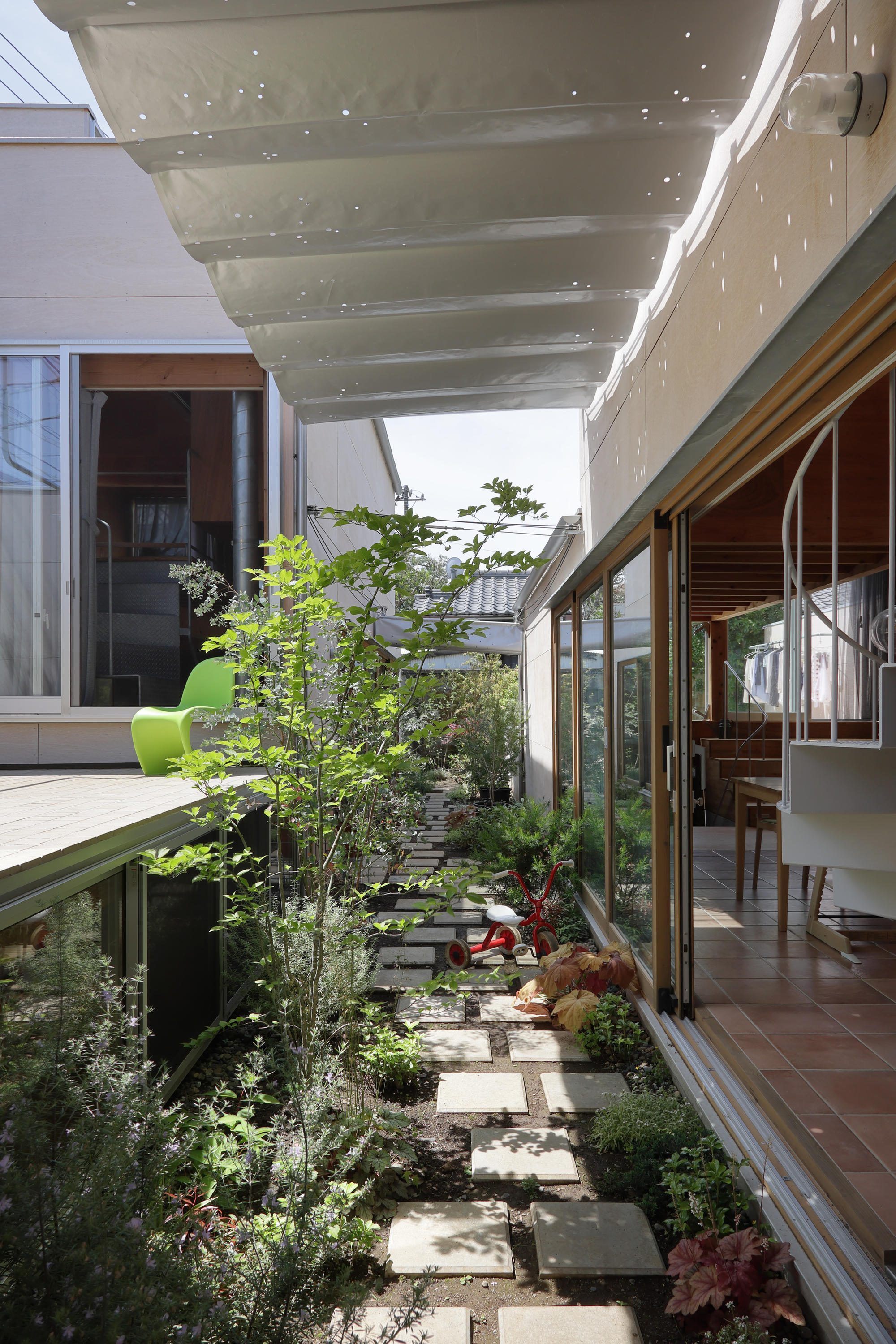 Narrow courtyard garden with stepping stones and planted beds beneath a perforated concrete canopy
