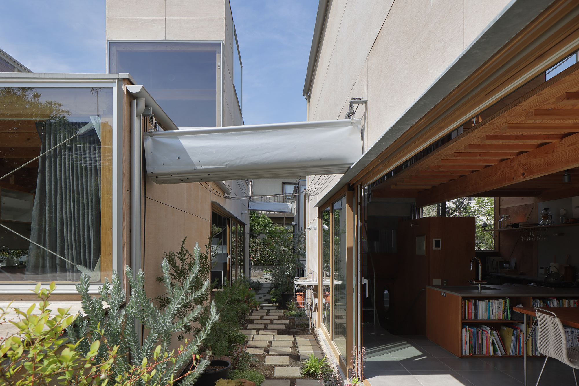 Courtyard view with white fabric canopy stretched between volumes and stepping stone path through plantings