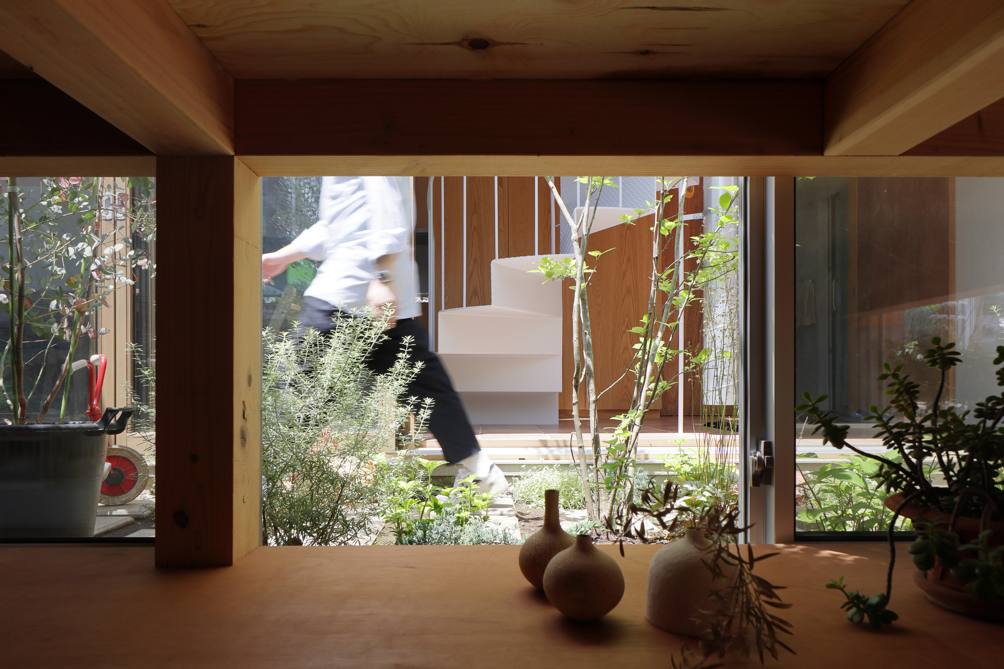 View through timber framed opening showing a person ascending exterior stairs with planted courtyard in foreground