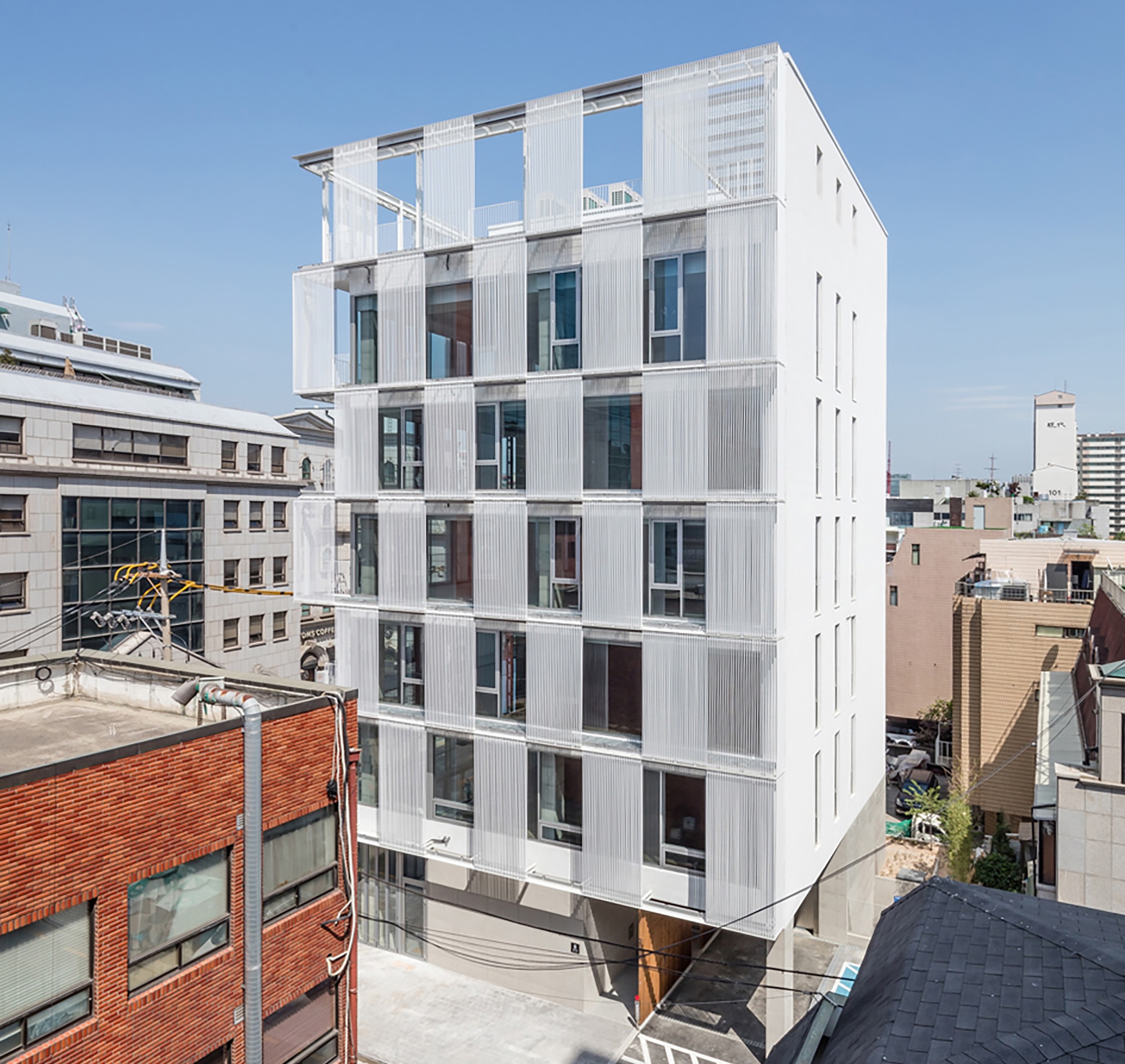 Elevated view of the white corrugated facade with staggered windows and balconies in a dense urban neighborhood