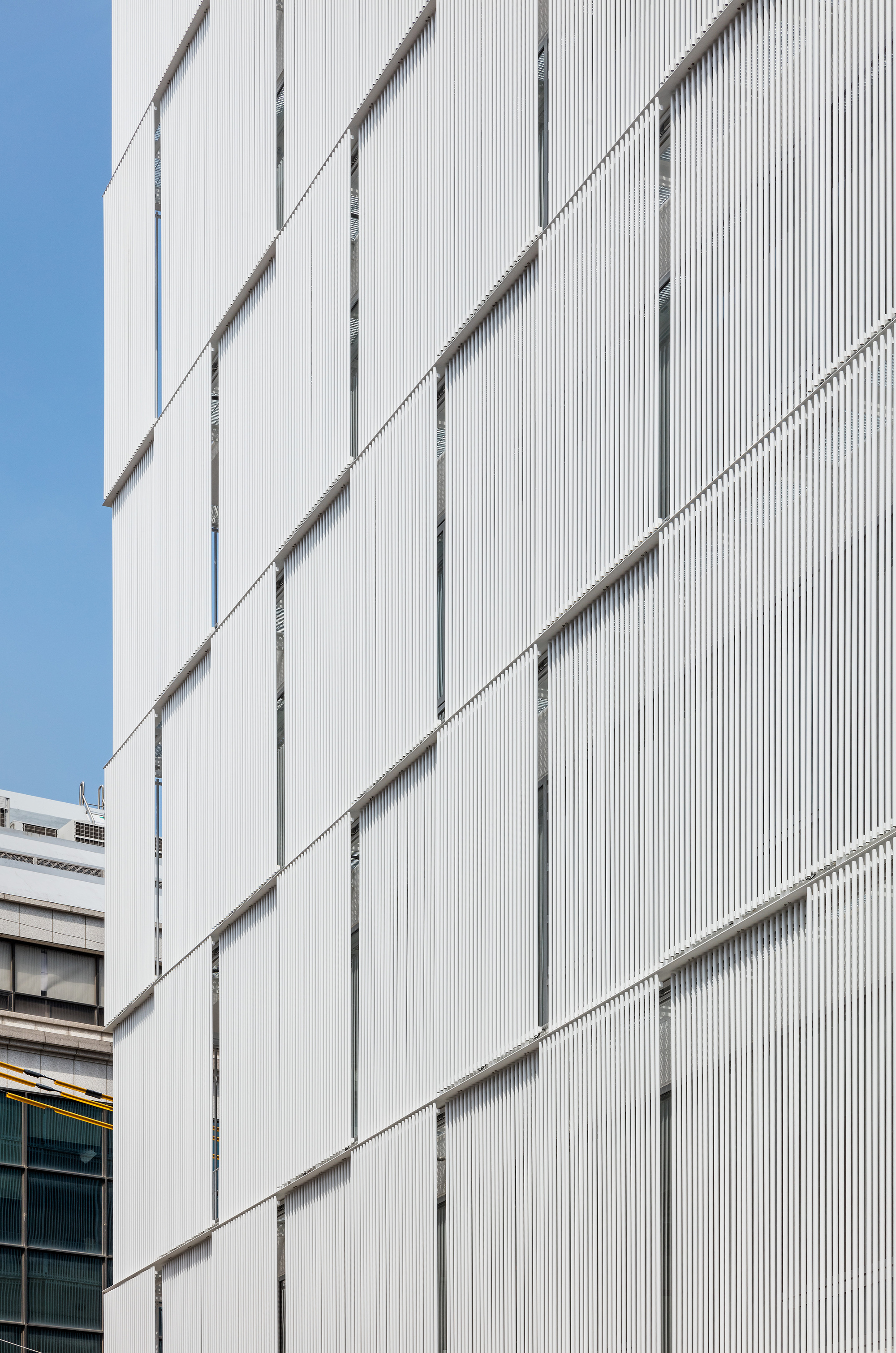 Close-up of the white fluted panels creating vertical shadows across the facade surface