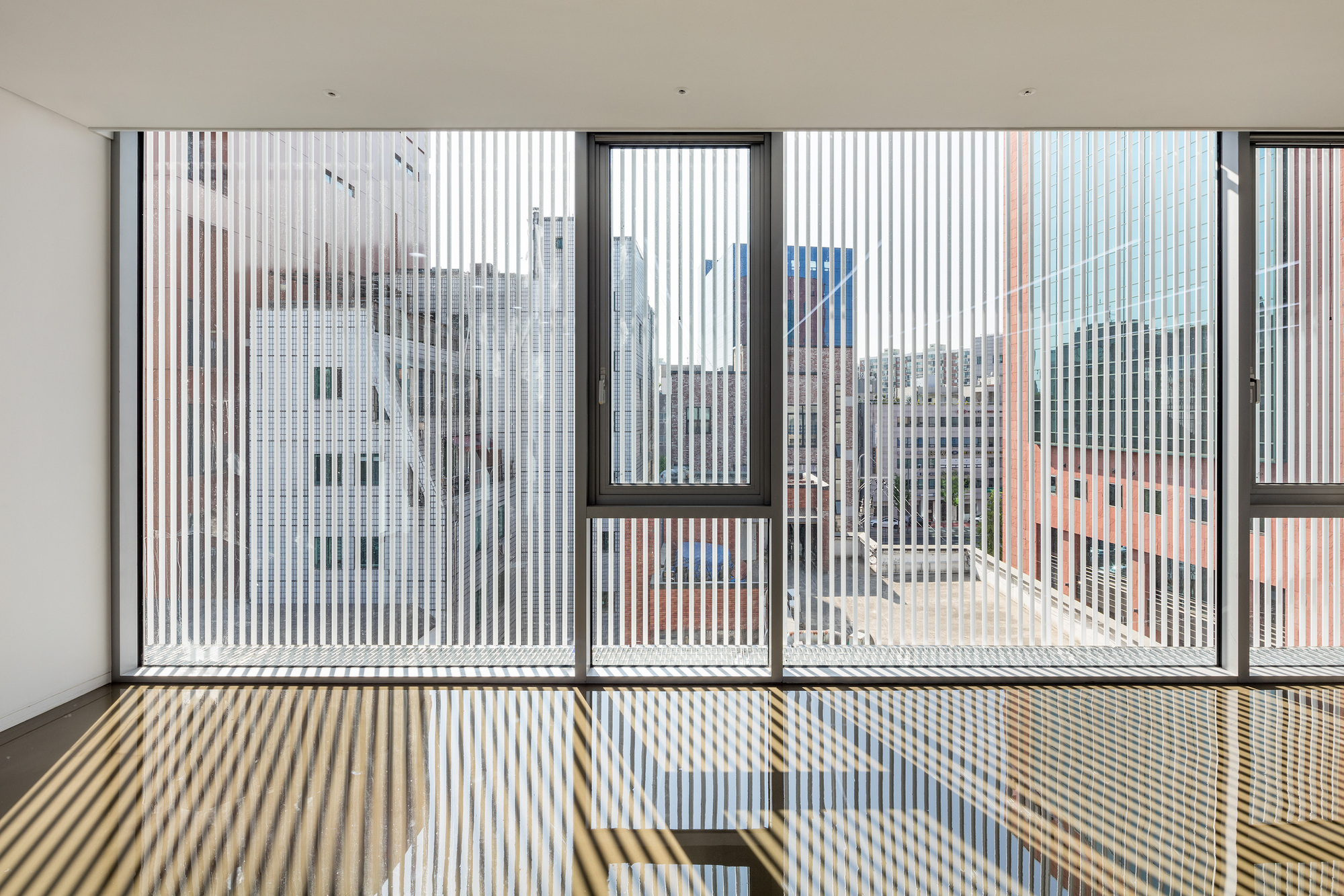 Interior view through vertical screen louvres casting striped shadows on the floor and balcony