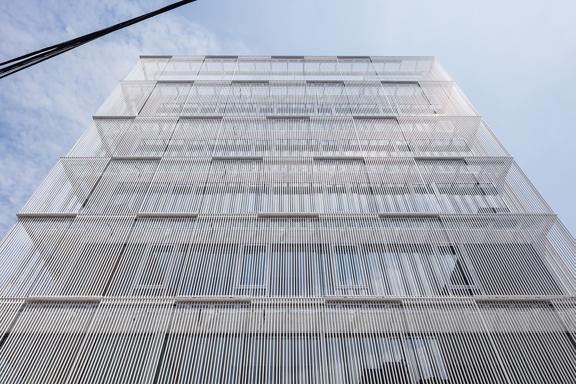 Upward view of a white metal louvered facade with stepped horizontal floor plates against blue sky