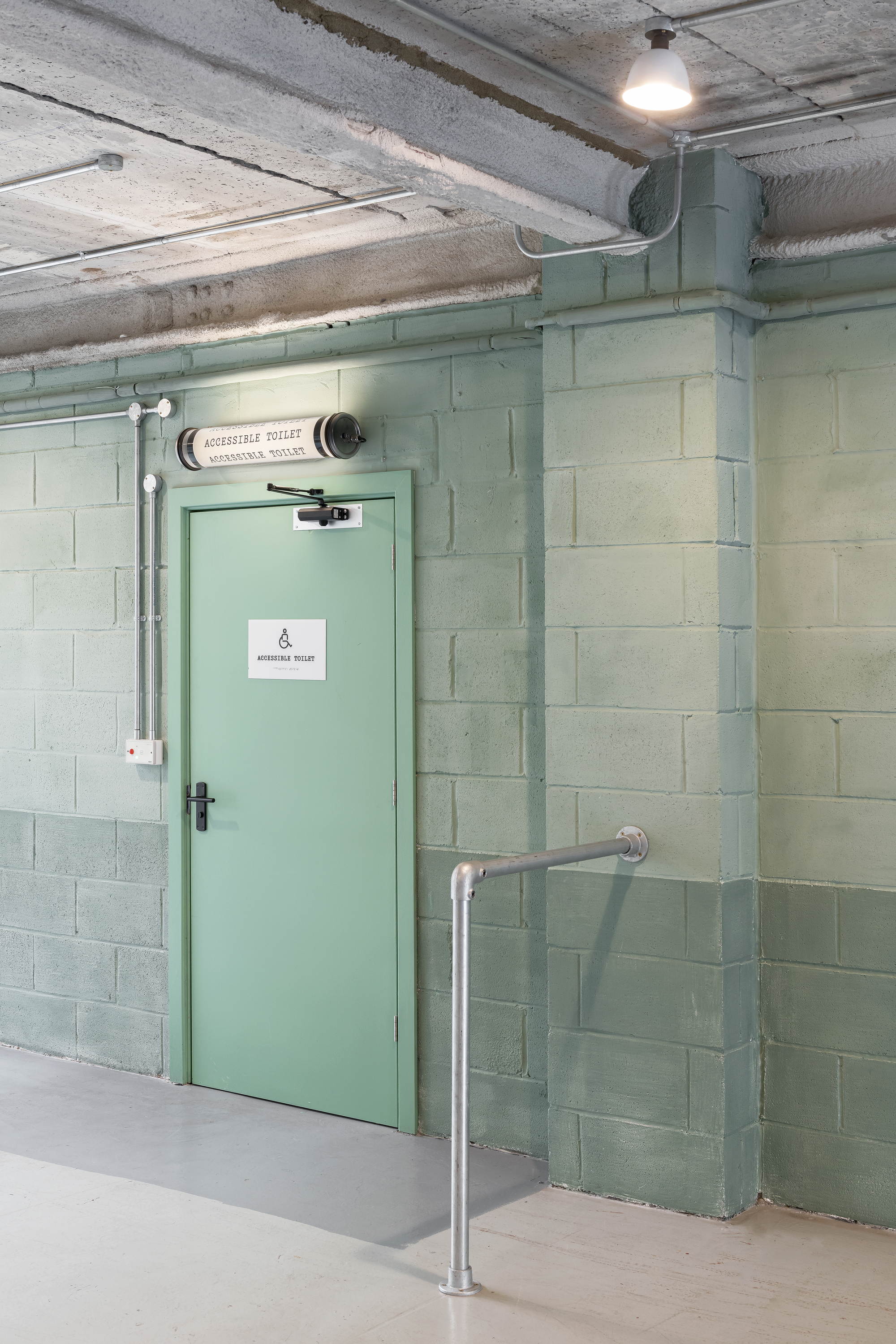 Mint green steel door with exposed conduit and concrete block walls under an industrial ceiling
