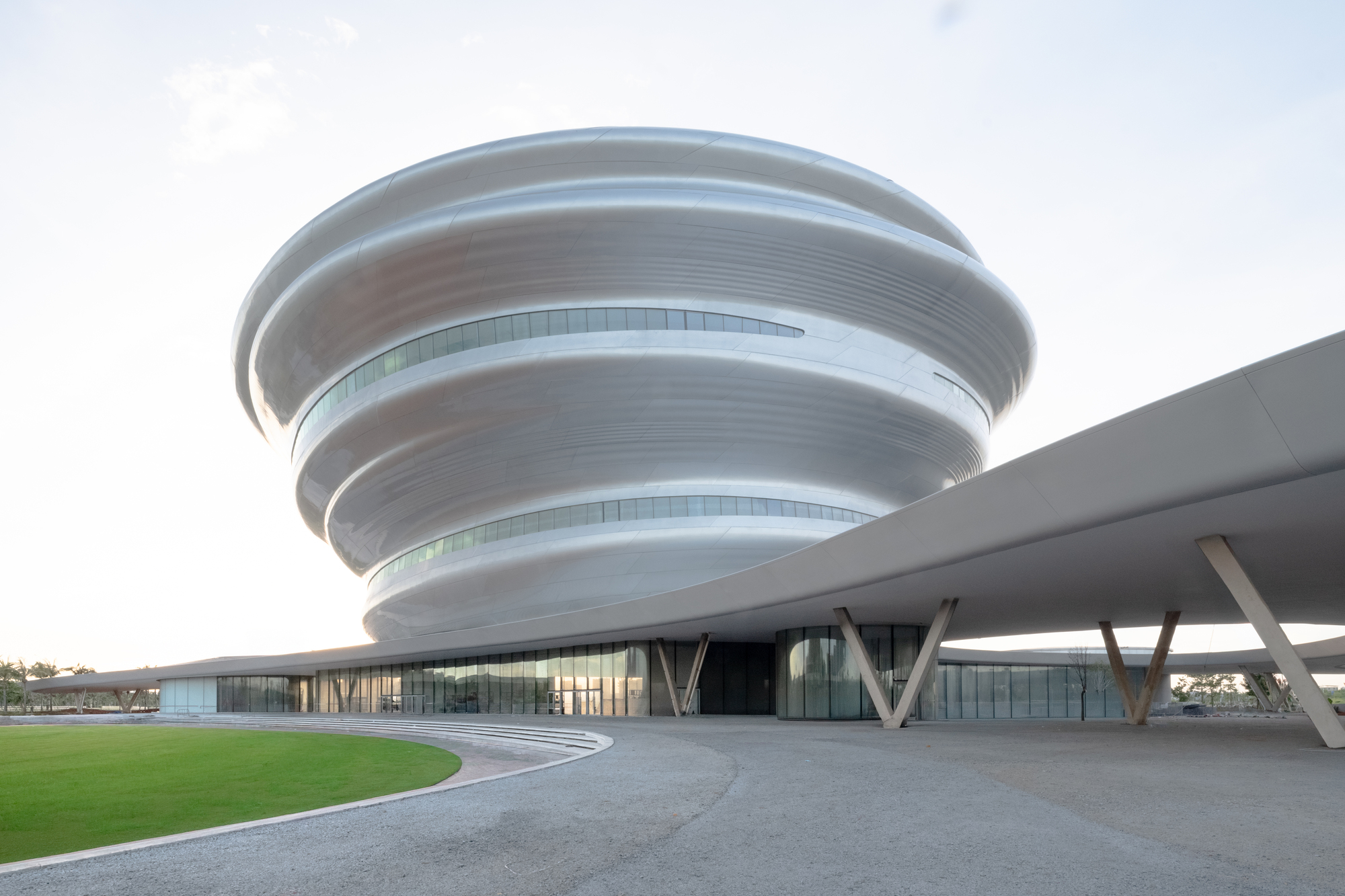 Ground-level view of the spiral facade rising above angled V-shaped columns with a lawn in foreground