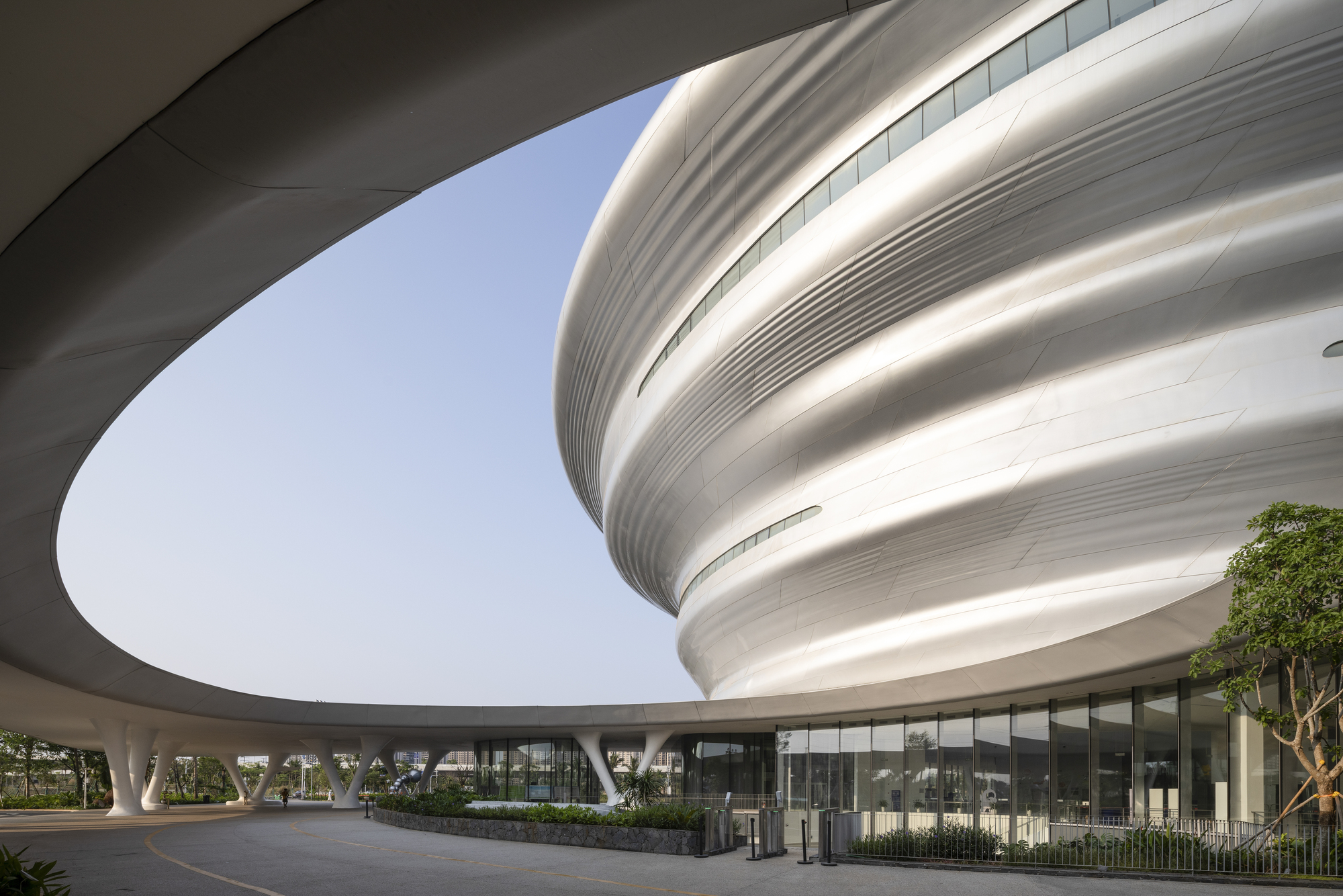 View beneath the curved canopy showing the spiraling tower volume framed by angled structural supports and planted beds