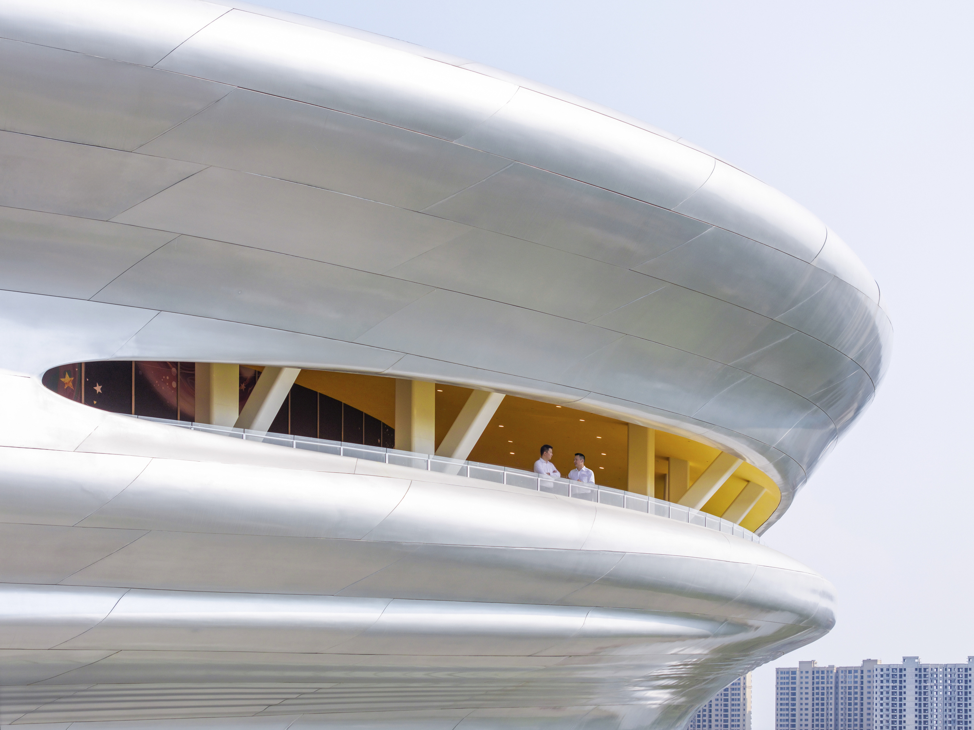Close-up of two curved balcony levels with two visitors standing at the railing under an overcast sky