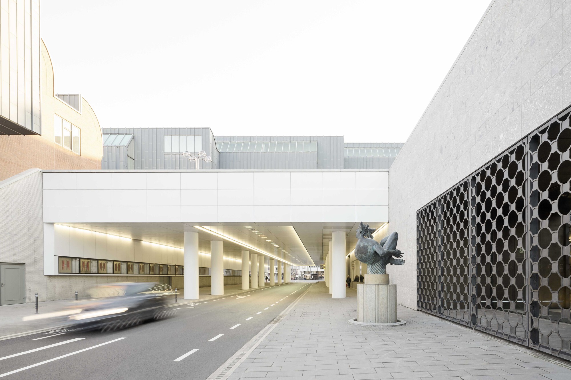 White bridge structure spanning a roadway with round columns and patterned metal screen wall in daylight