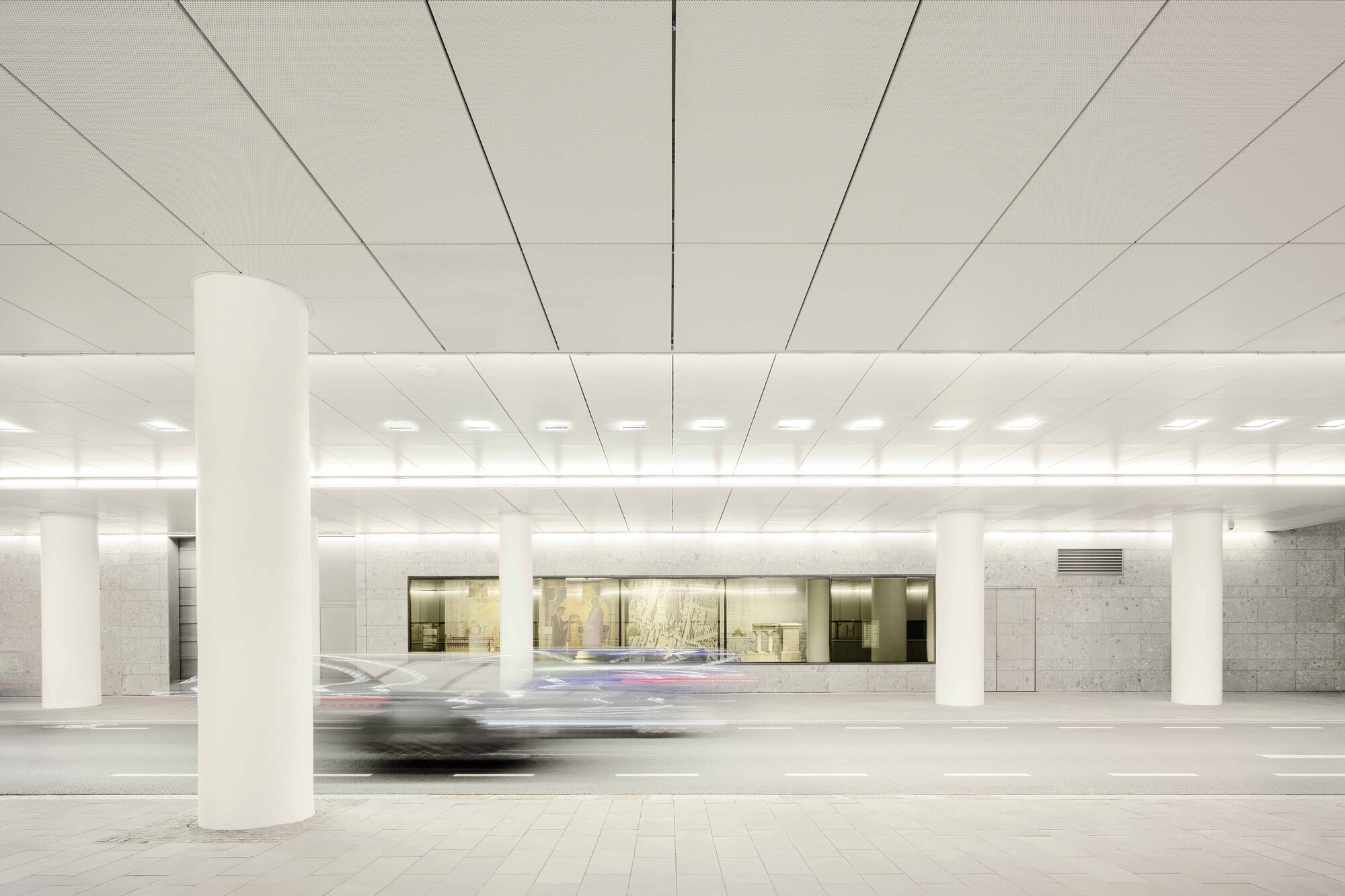 Underground parking level with white columns and recessed lighting as a car passes in motion blur