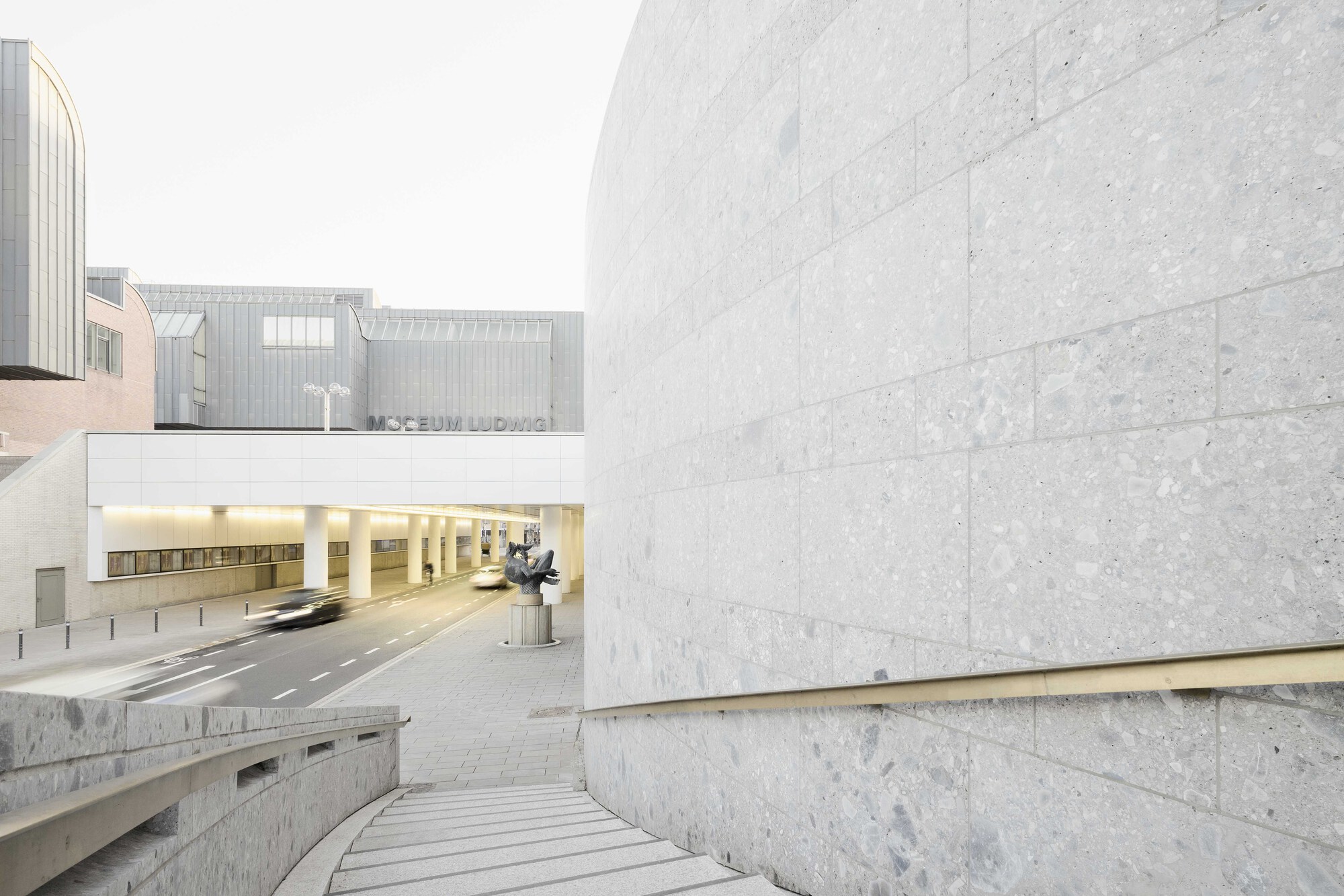 Stone steps descending between limestone walls toward an illuminated tunnel opening with sculpture visible beyond
