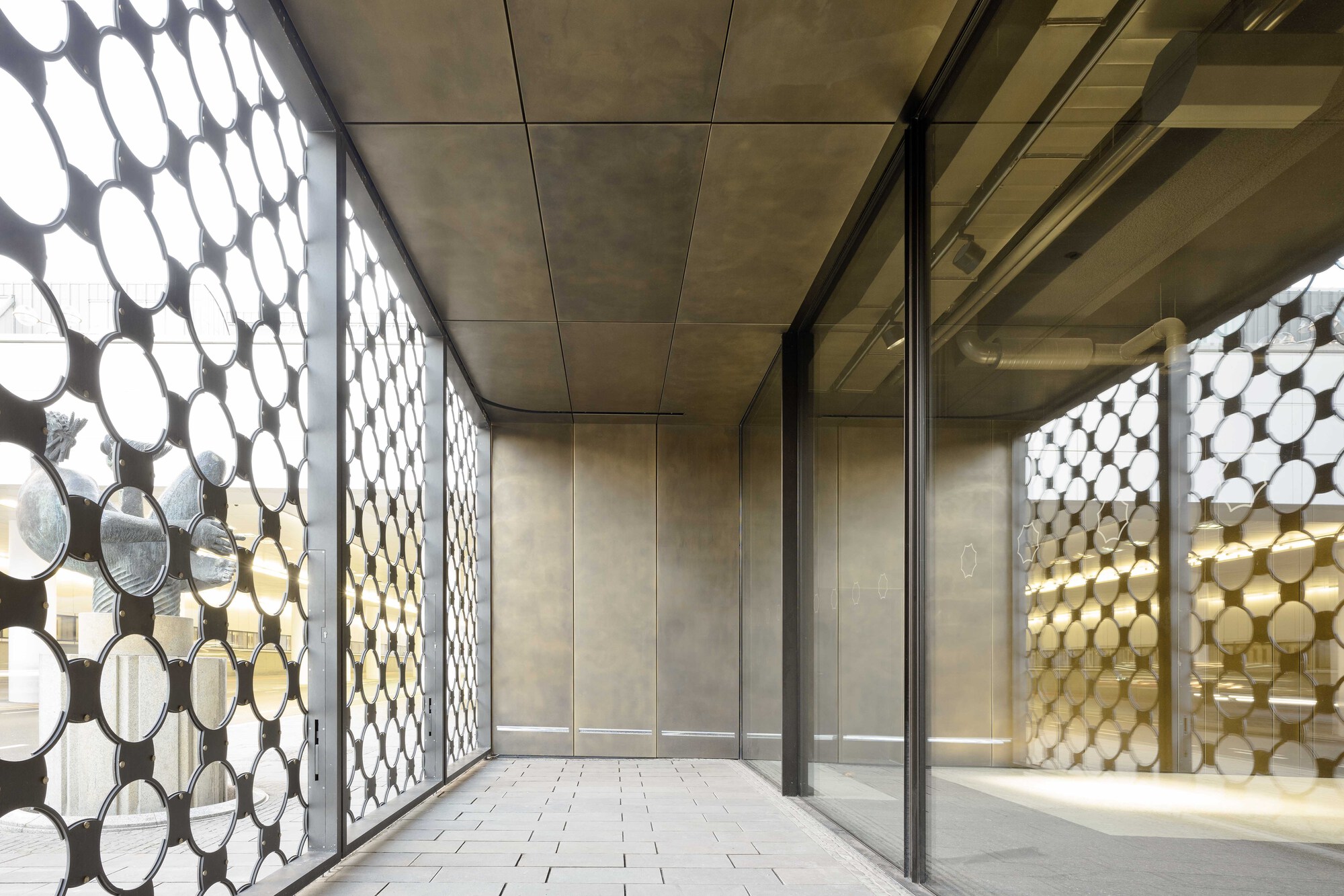 Interior corridor with perforated circular metal screens flanking both sides and polished stone flooring