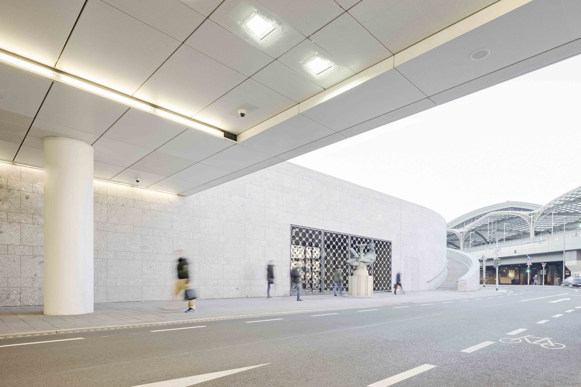 Interior passage with dropped ceiling panels and cylindrical columns alongside a curved stone wall
