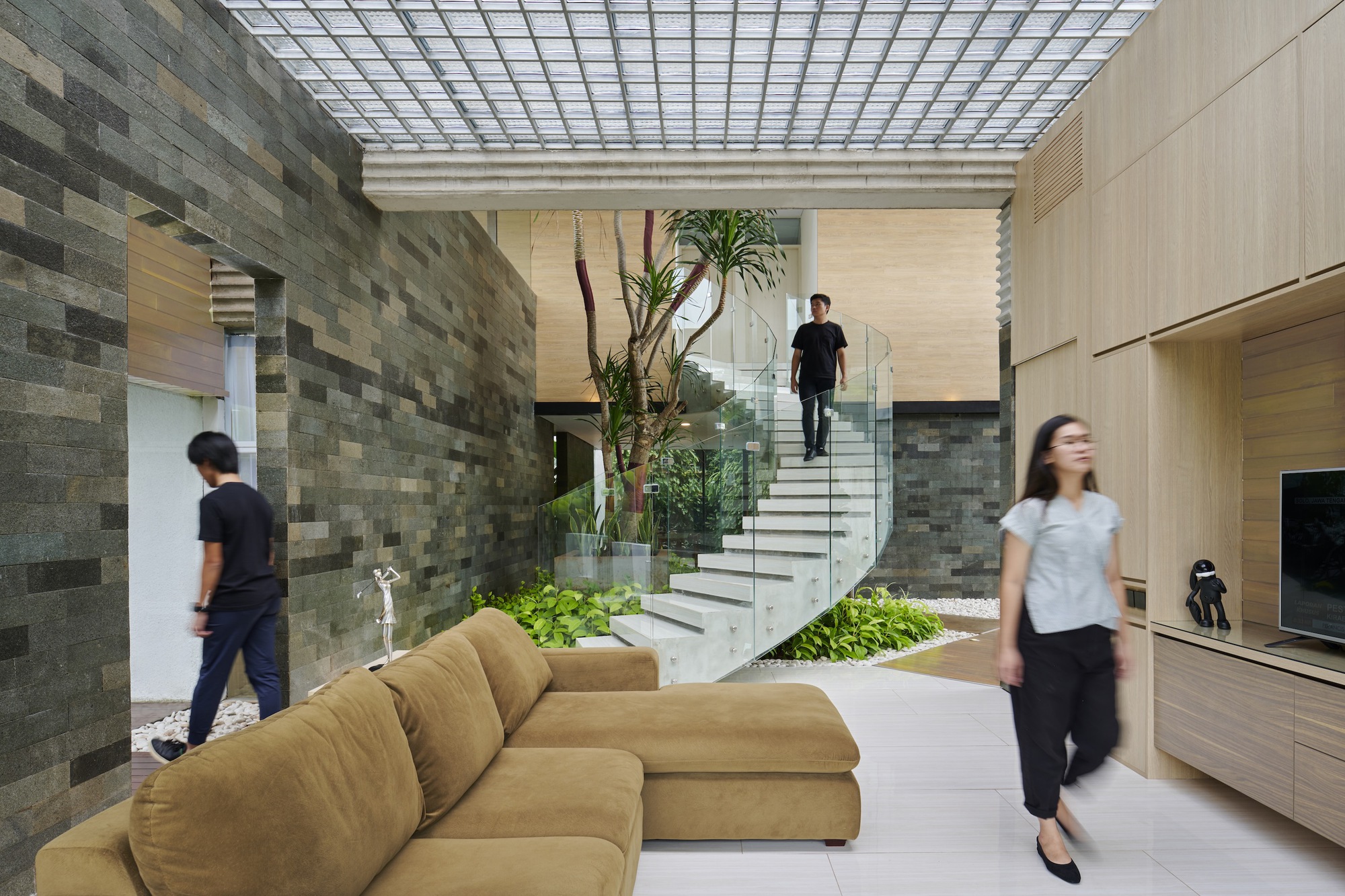 Living room with gridded skylight above stone accent wall and floating staircase flanked by planted beds