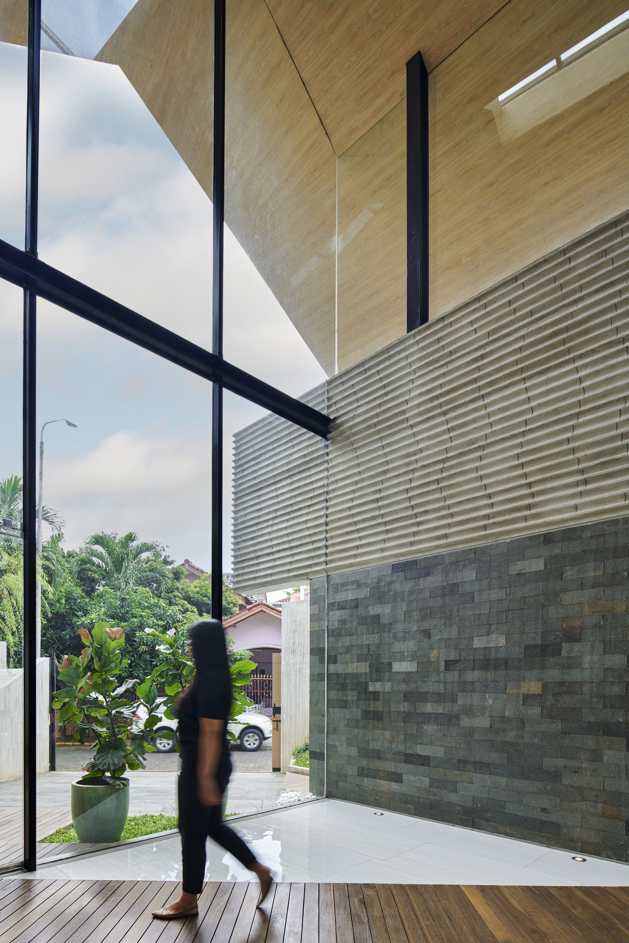 Entry threshold with horizontal louvered screen and resident walking past the variegated stone wall