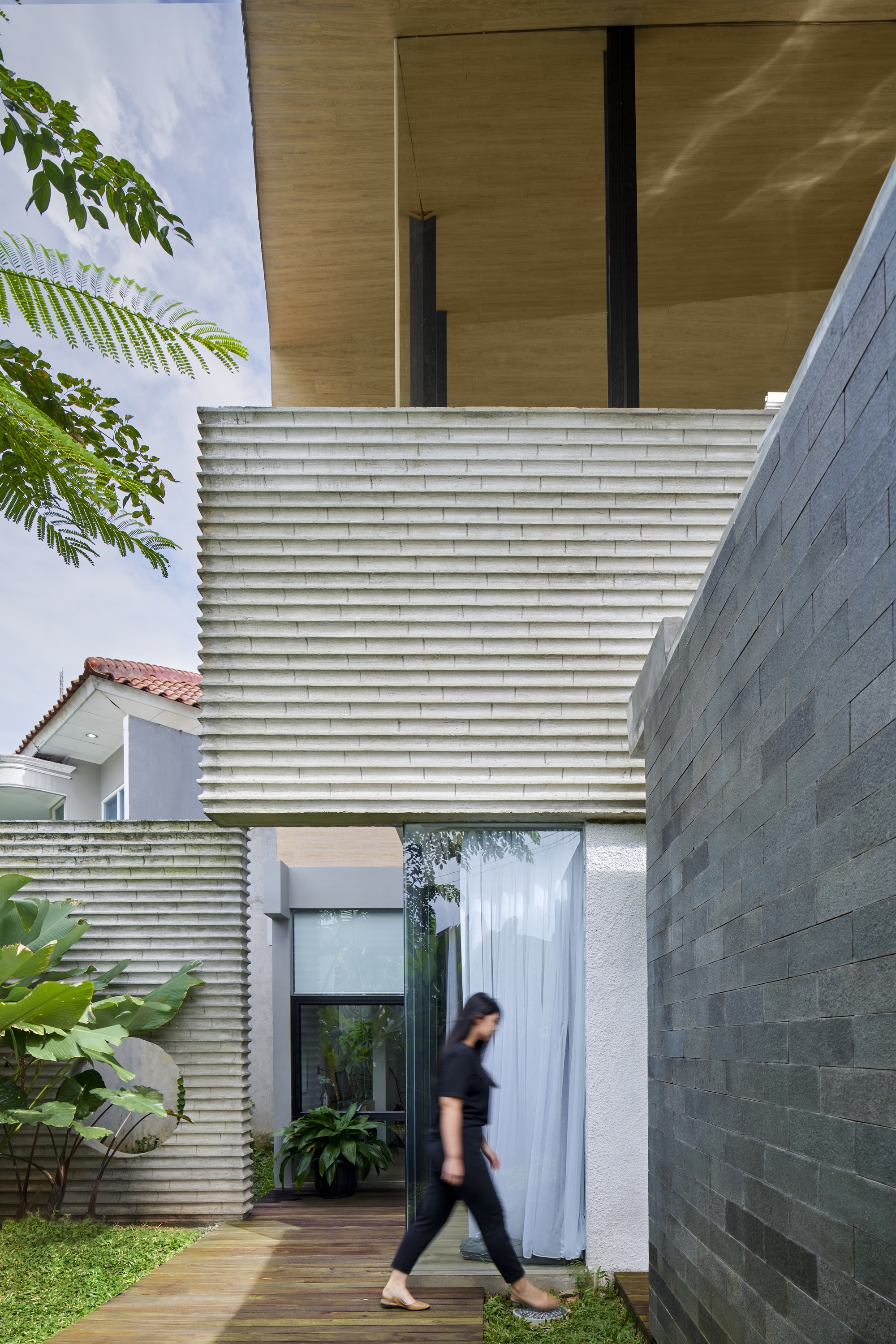 Timber deck walkway beneath cantilevered plywood soffit with horizontal louvered screen and person in motion