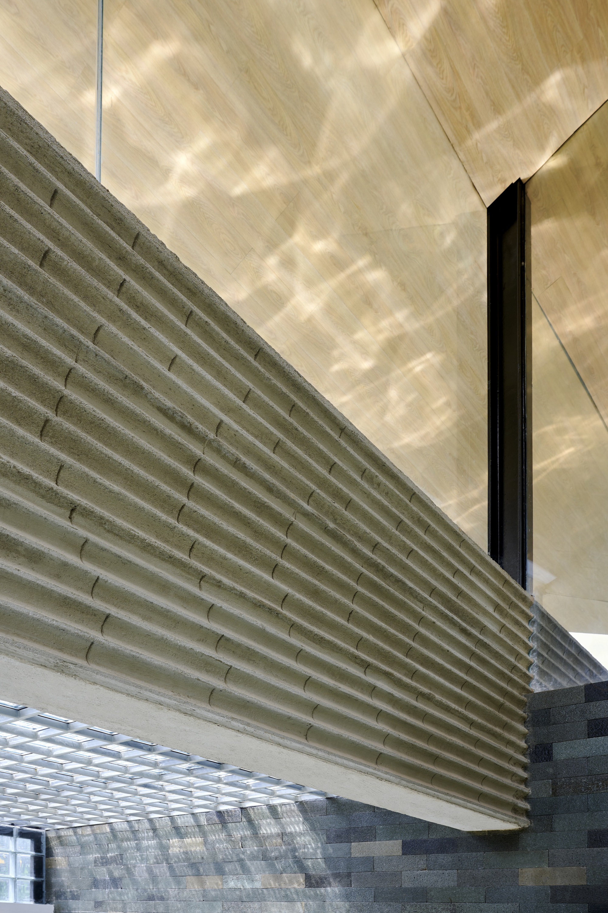 Close-up of horizontal concrete louvered screen meeting plywood soffit with dappled shadows falling across surfaces