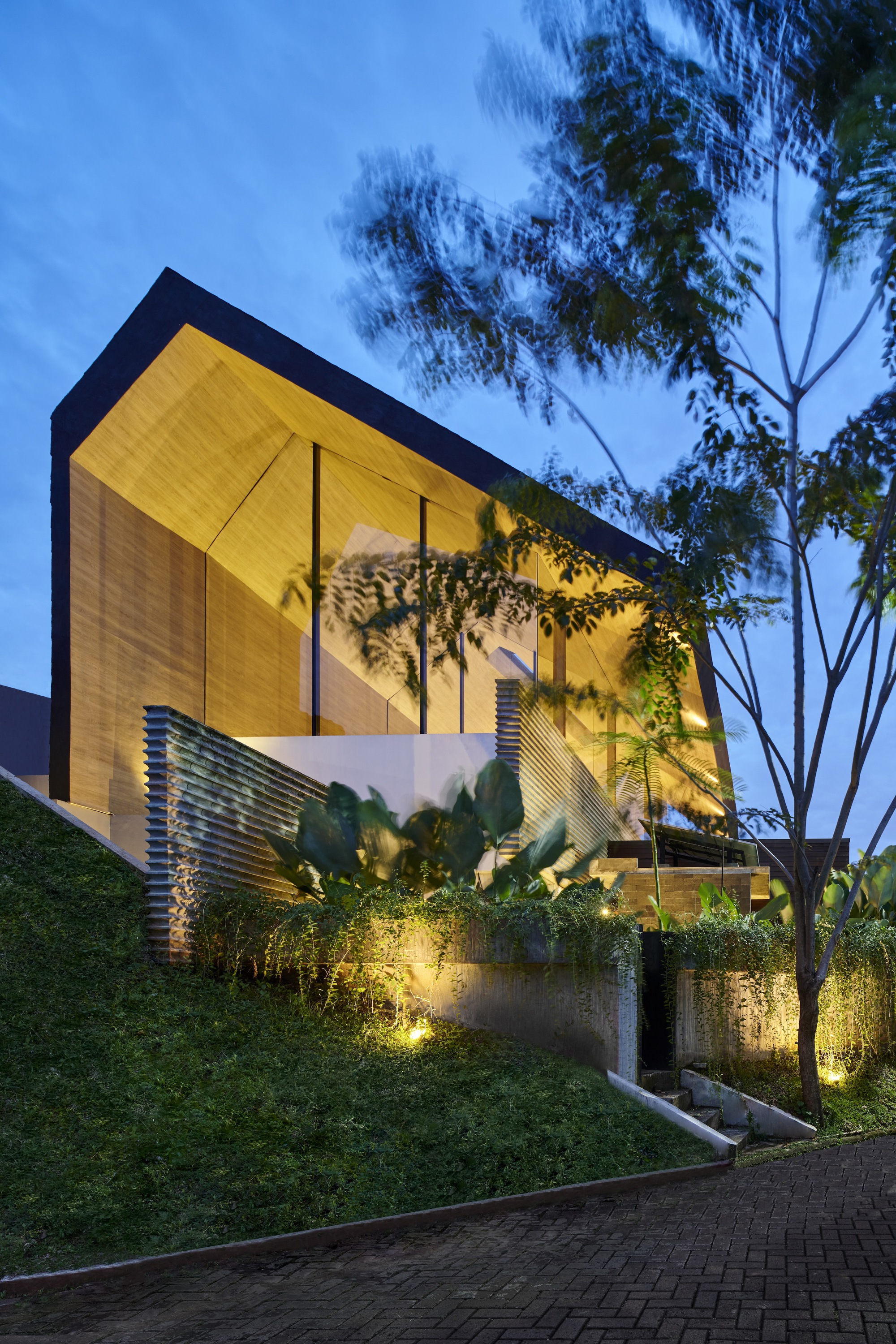 Facade showing the cantilevered timber-paneled upper floor above planted terraces at twilight