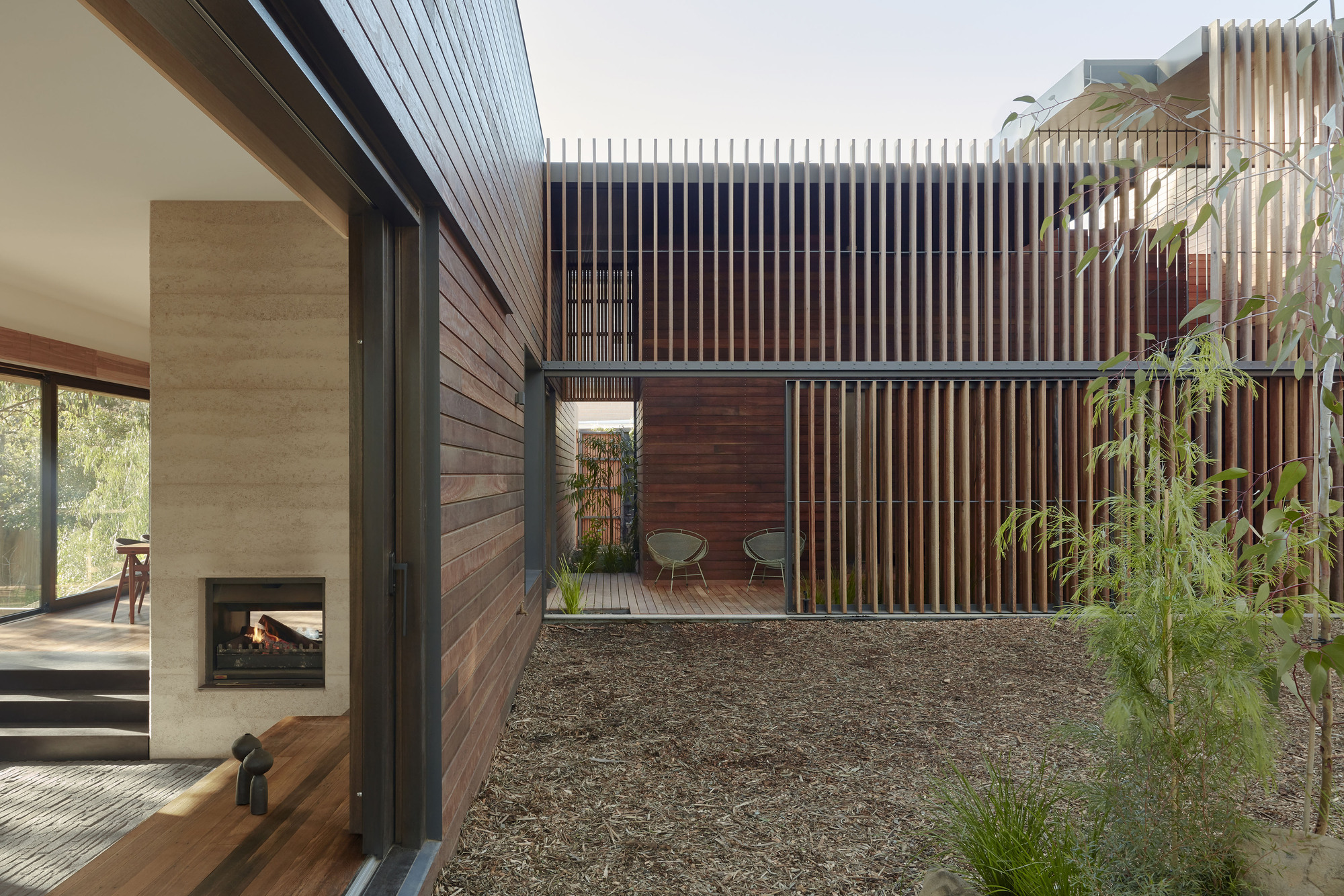 Gravel courtyard enclosed by horizontal timber cladding and vertical wood slat screens with bamboo