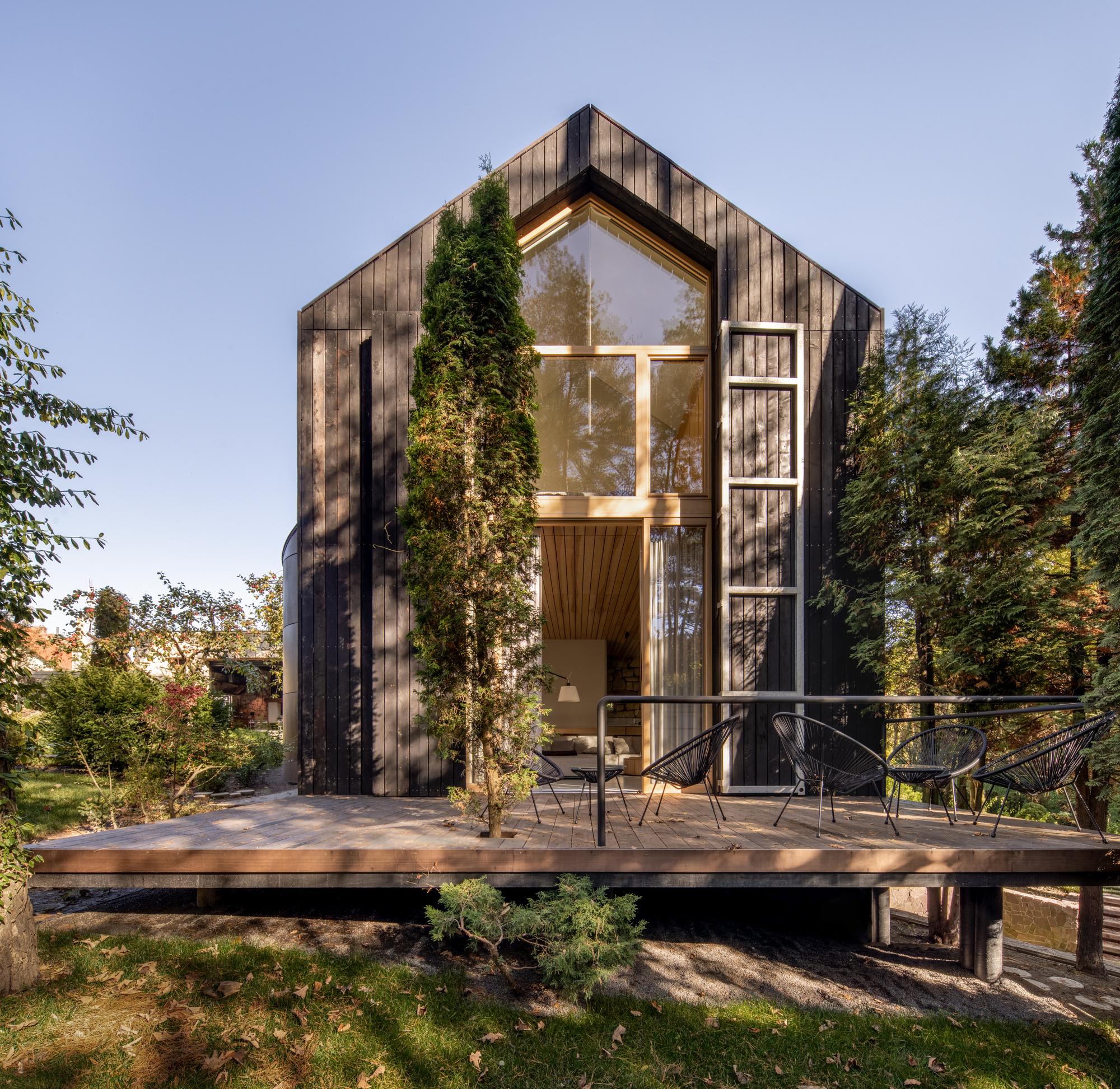 Gabled timber facade with large glazed opening above a raised deck platform at dusk