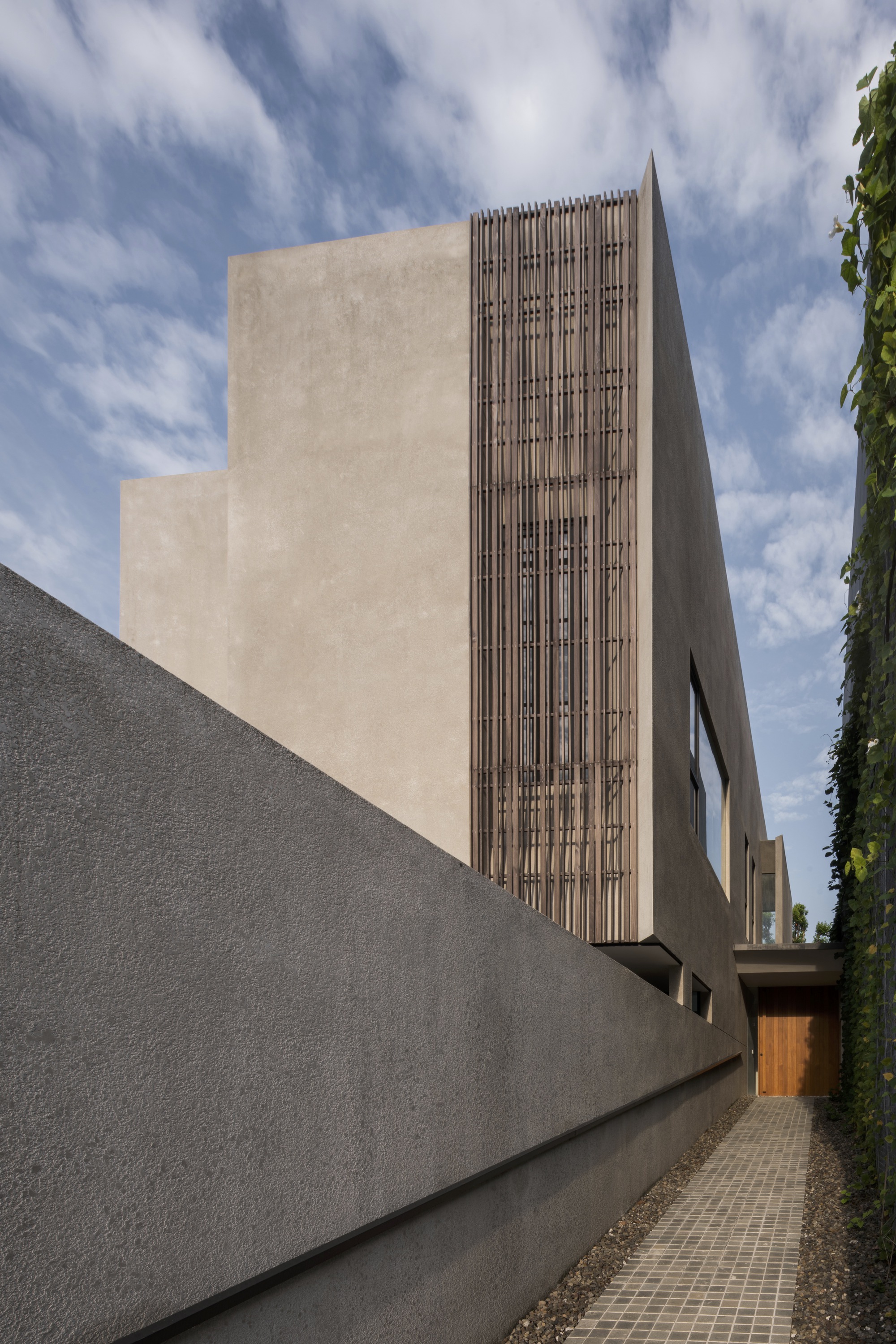 Side elevation showing the vertical timber screen panel against smooth plaster volumes under scattered clouds