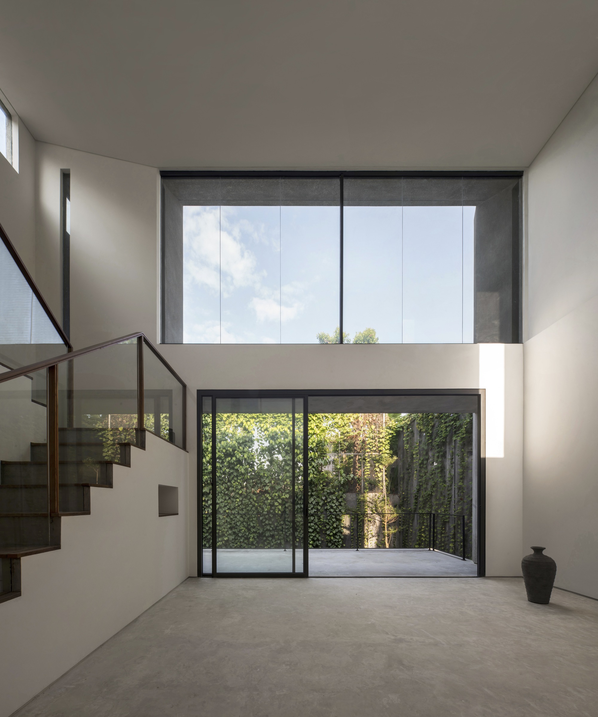 Double-height interior space with steel-framed glazing overlooking a green courtyard wall