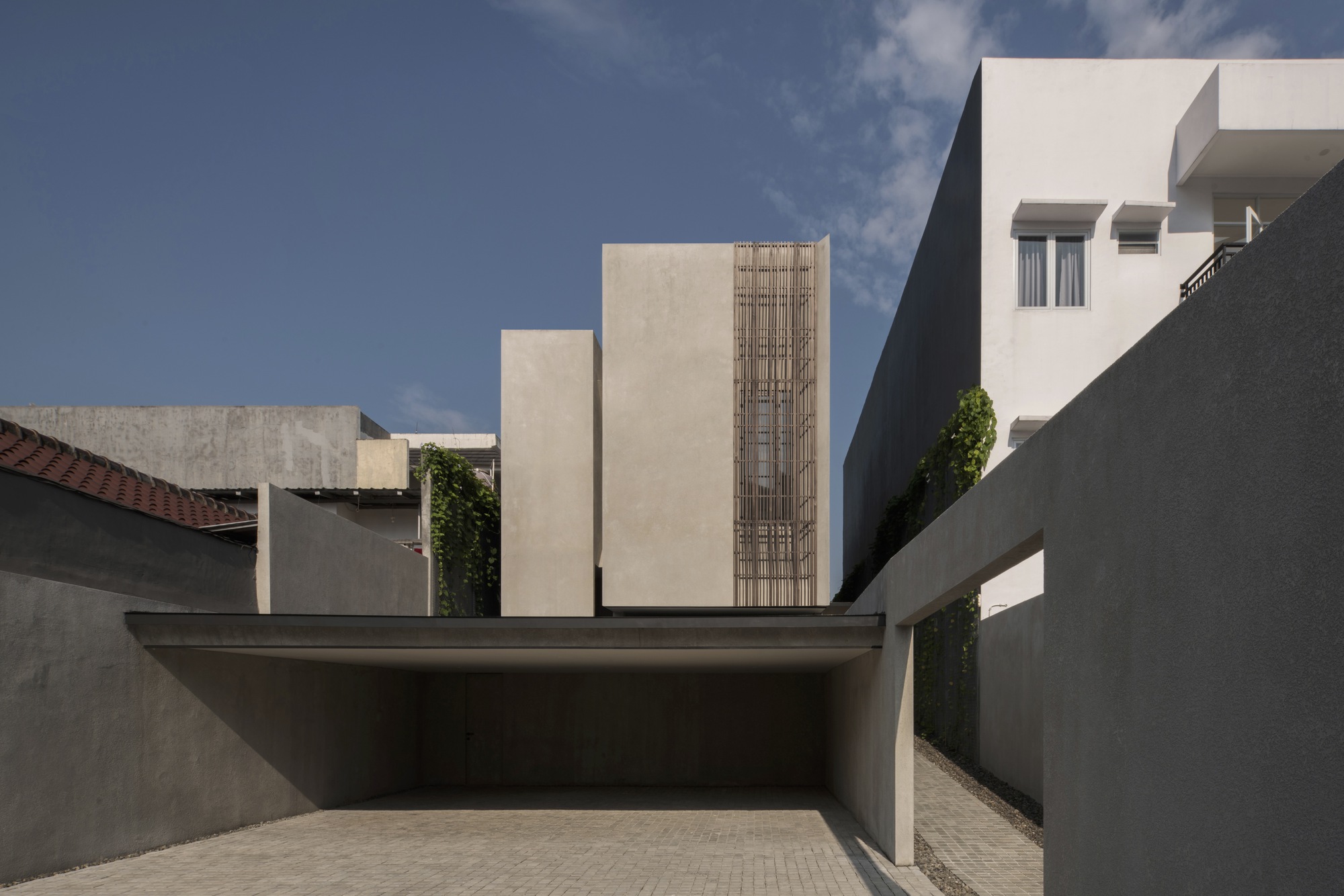 Entry courtyard framed by grey walls and the vertical timber screen under dramatic afternoon light