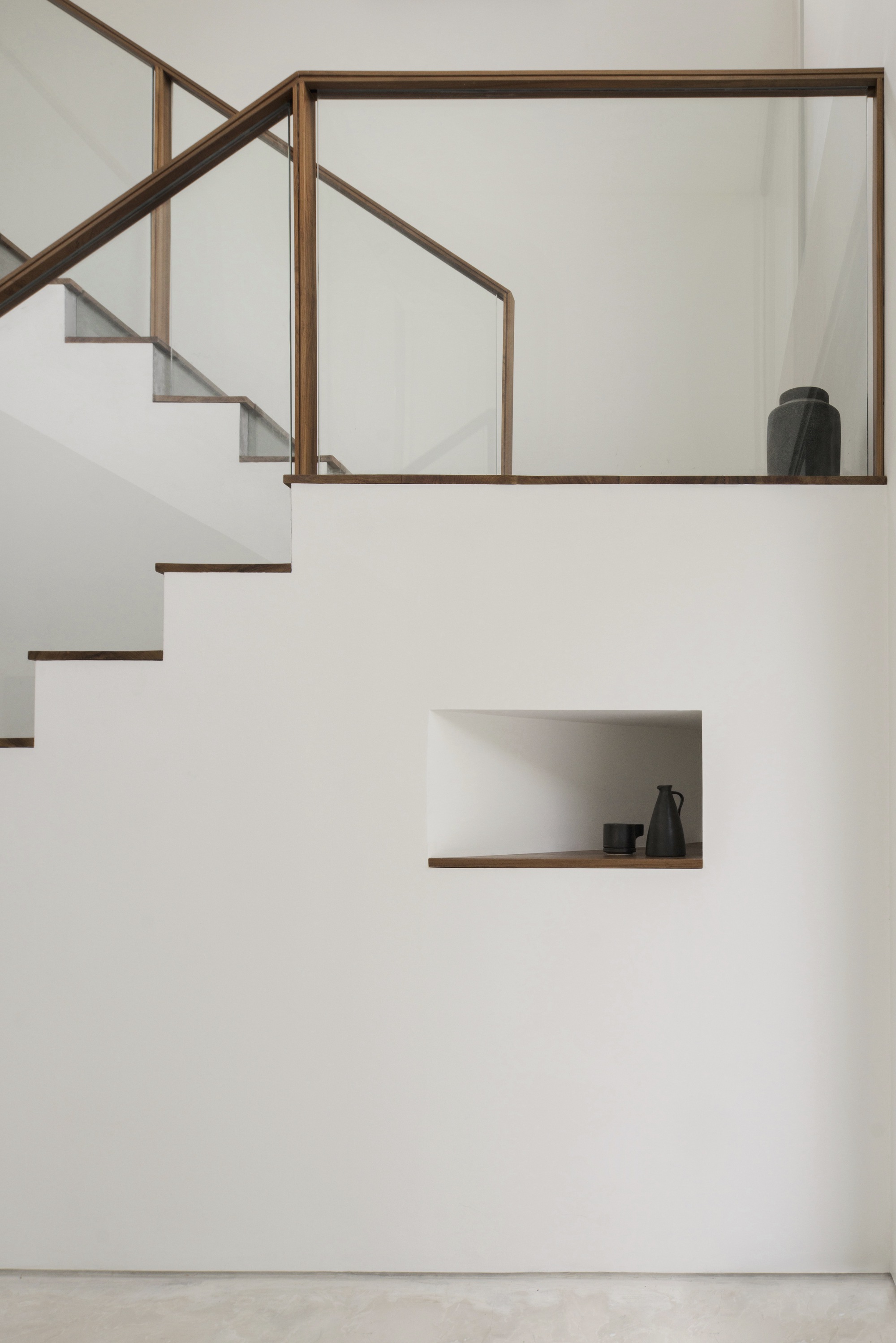 White staircase with timber-framed glass balustrade and recessed display niche holding ceramic vessels