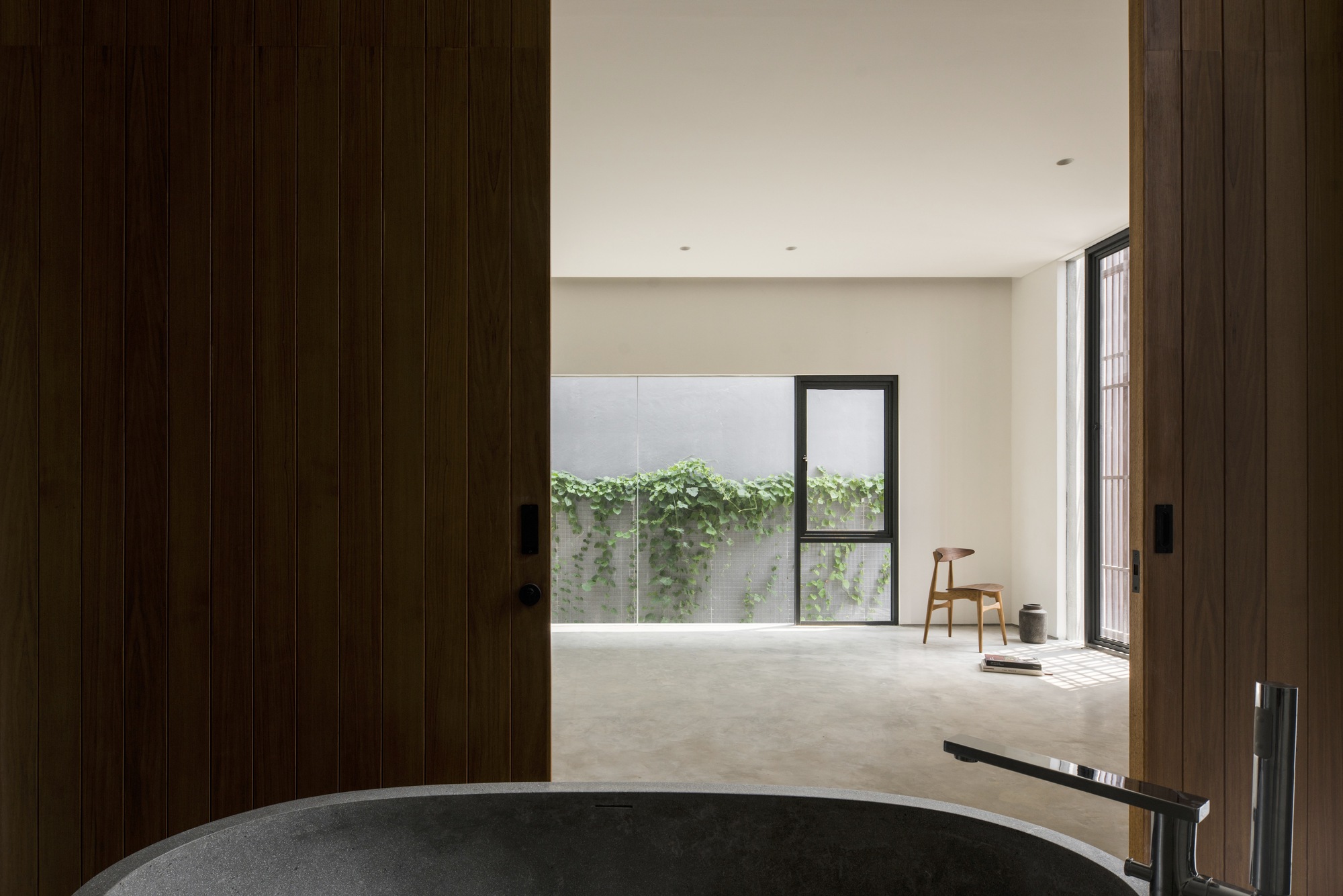 View through timber sliding doors to a polished concrete bathtub overlooking a planted courtyard