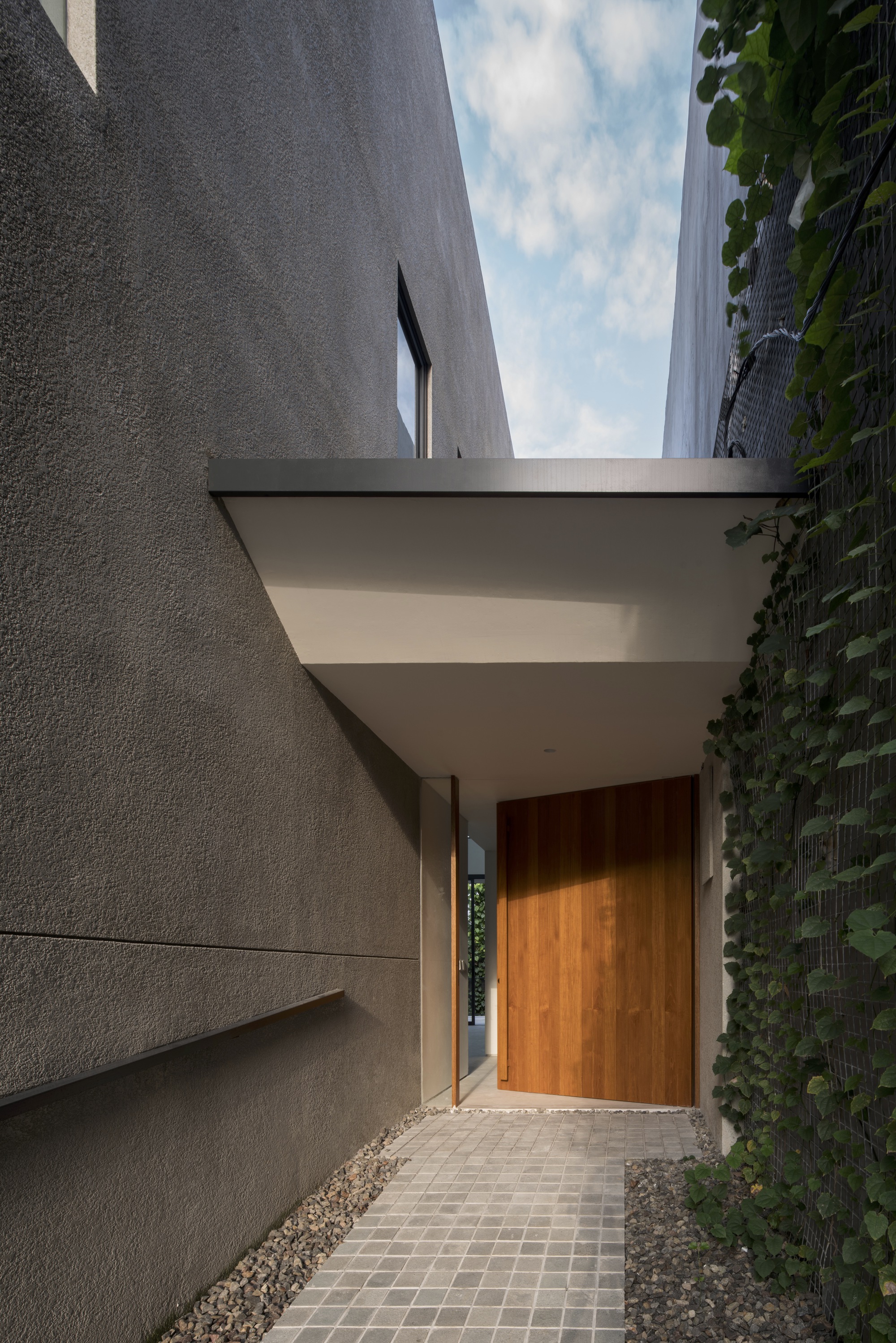 Entry path with wood door and canopy between textured concrete walls and a green wall at dusk