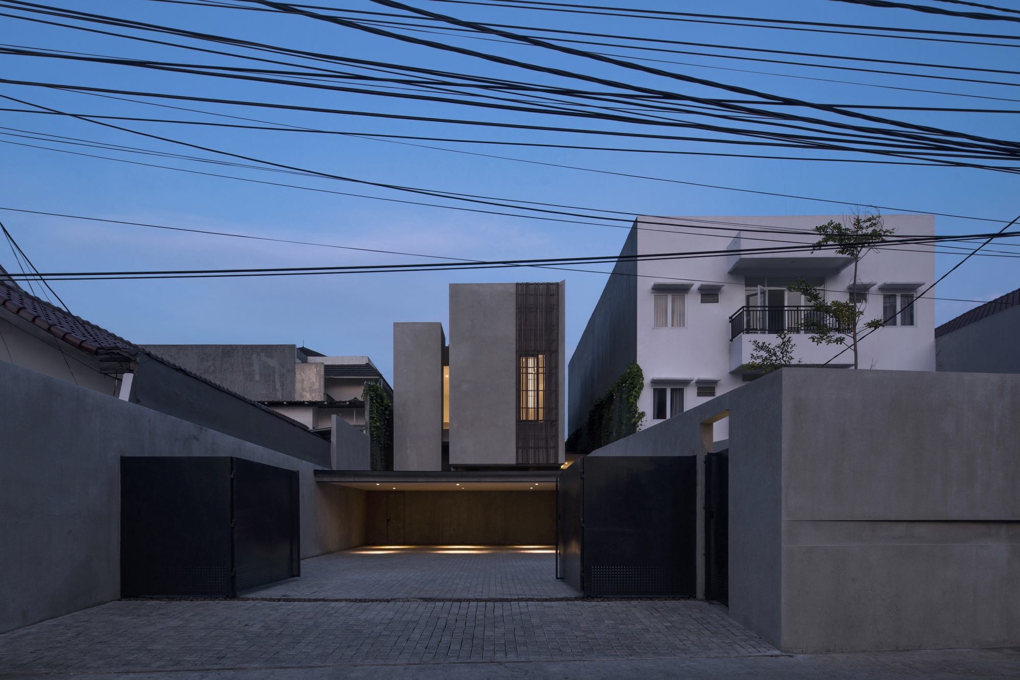 Street facade with illuminated carport and vertical window slots at twilight beneath overhead power lines