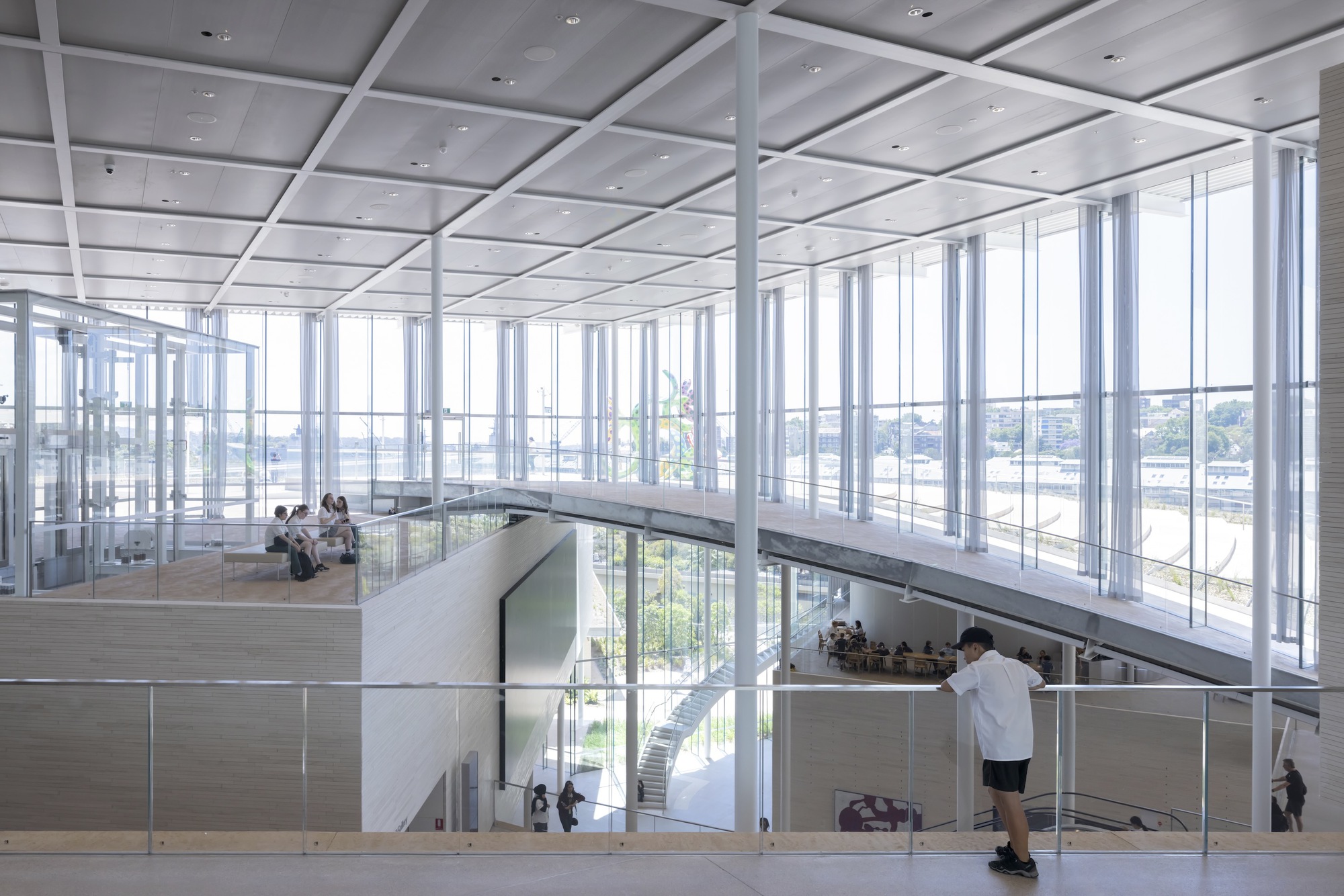 Upper level gallery with floor-to-ceiling glazing overlooking tiered spaces and visitors below
