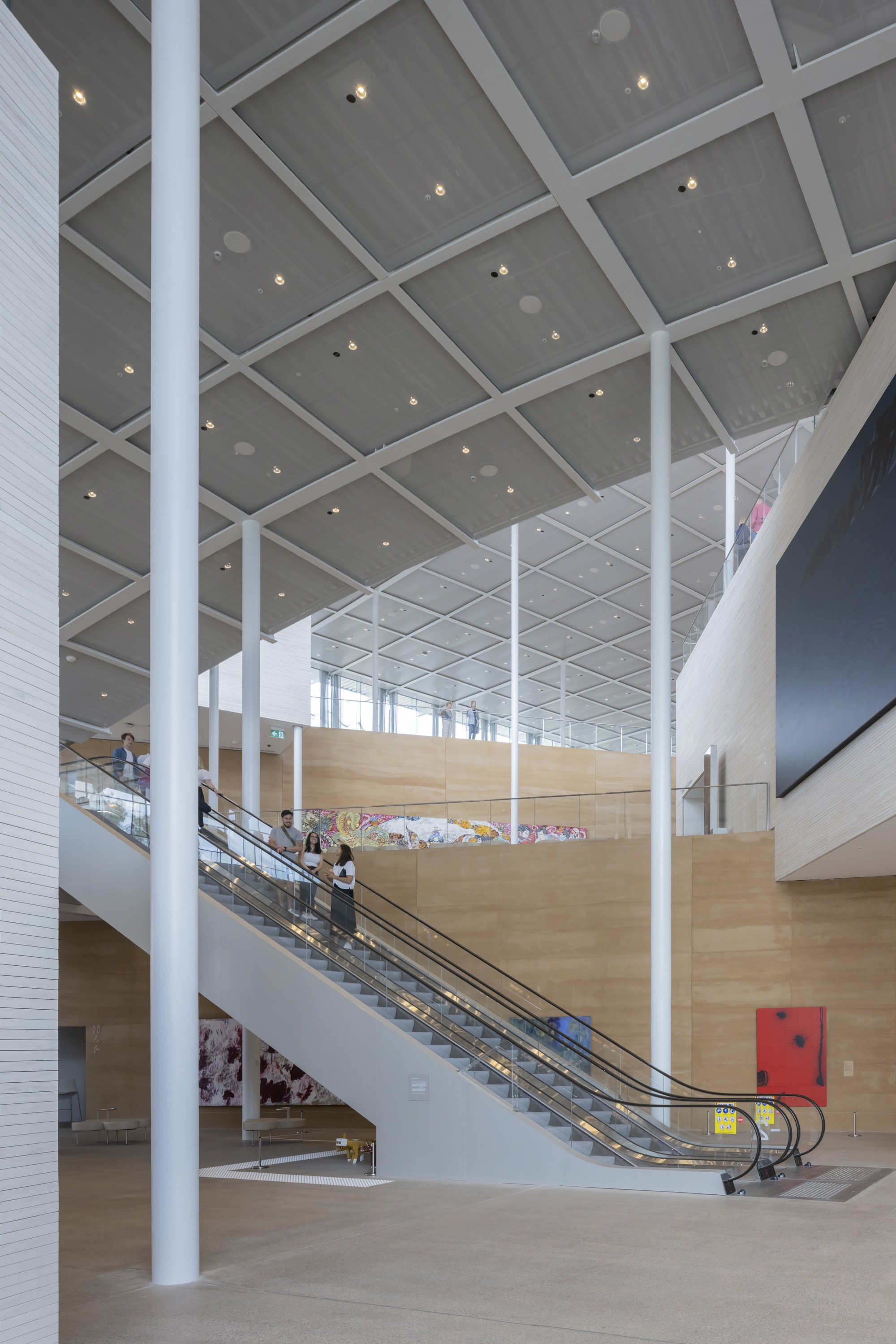 Interior atrium with escalators rising between white columns under a grey coffered ceiling with recessed lighting