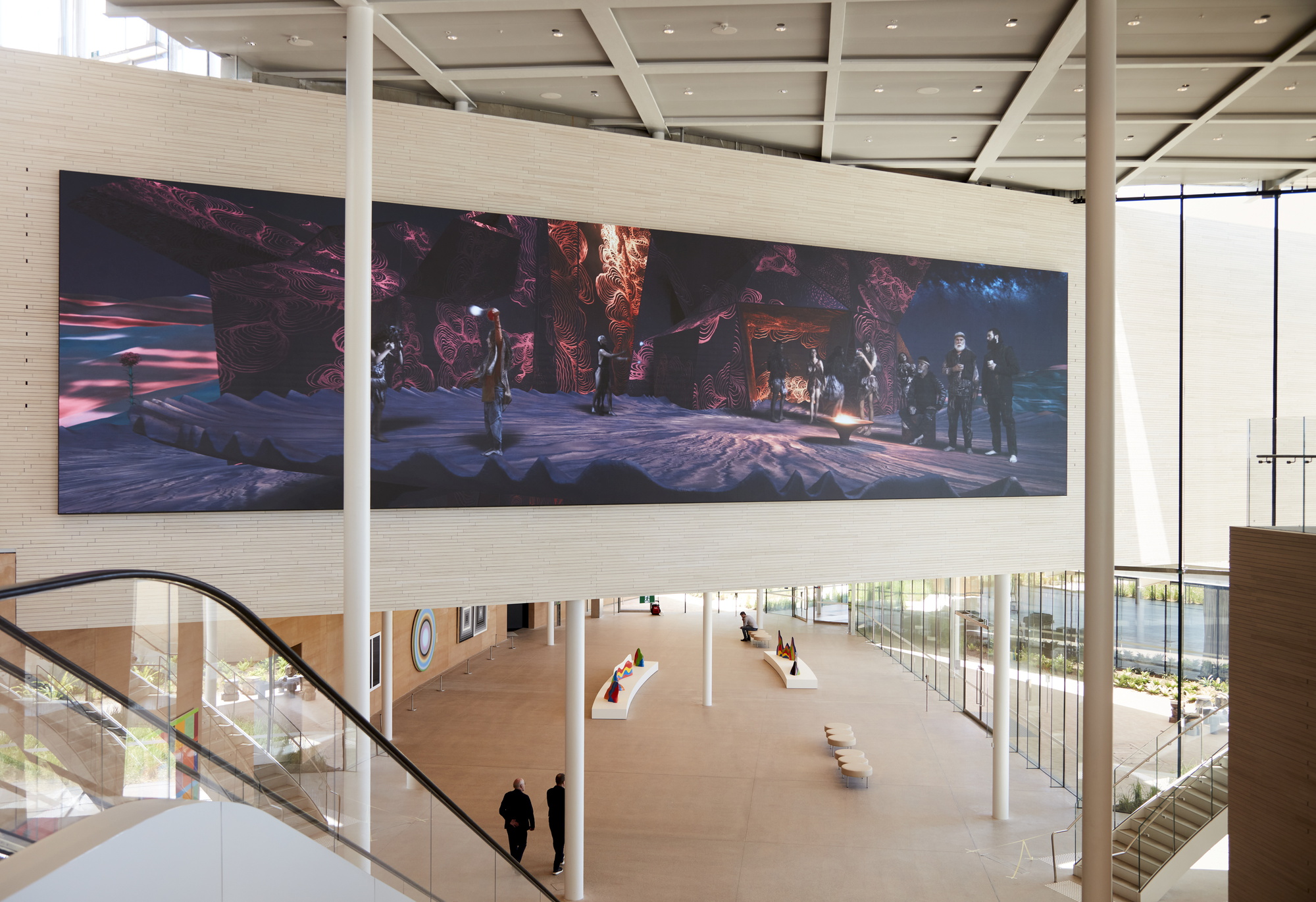 Double-height gallery space with a person descending a curved staircase beneath a wide horizontal video projection