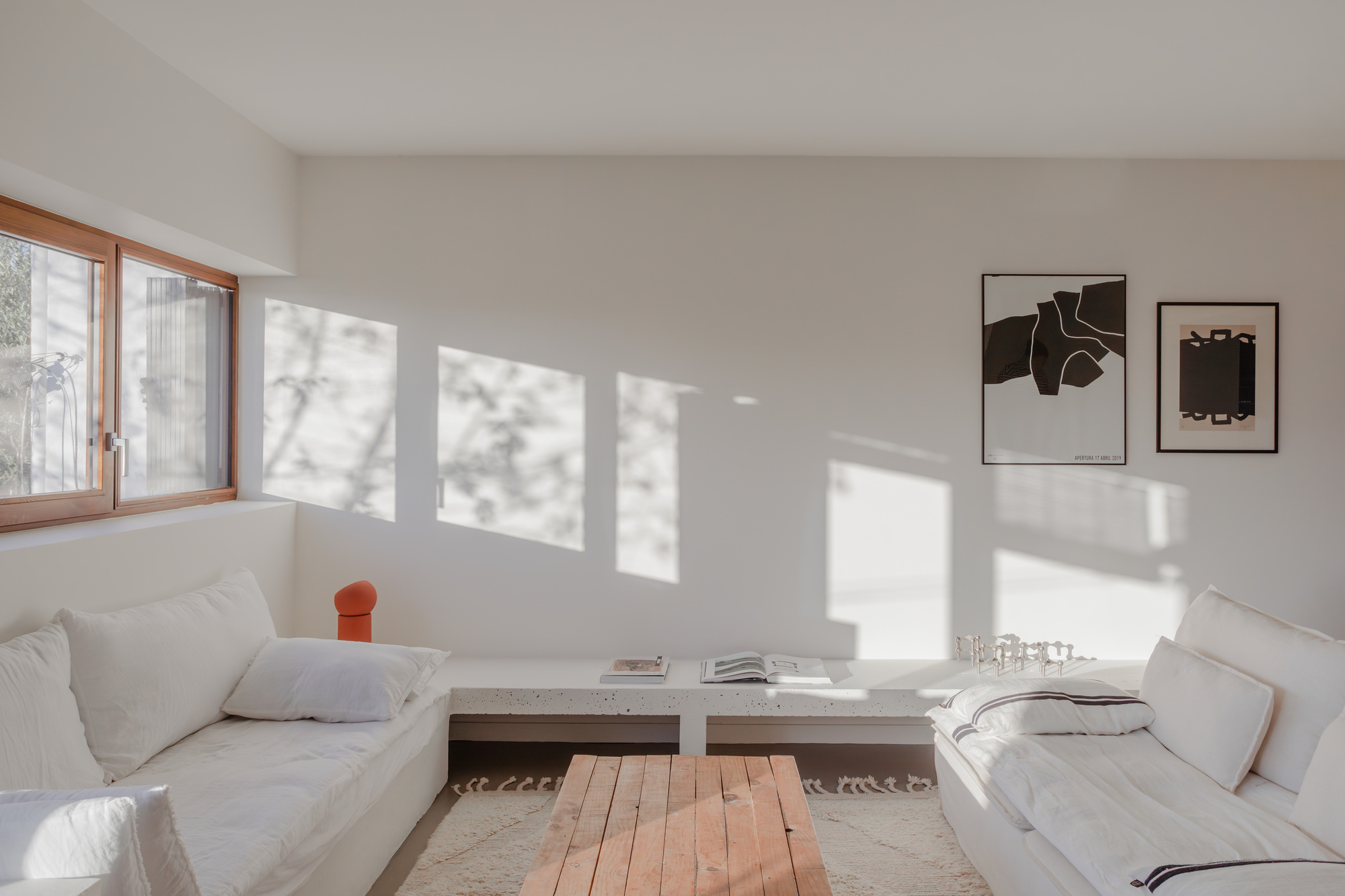 White interior living room with timber-framed windows casting sharp rectangular shadows across the floor