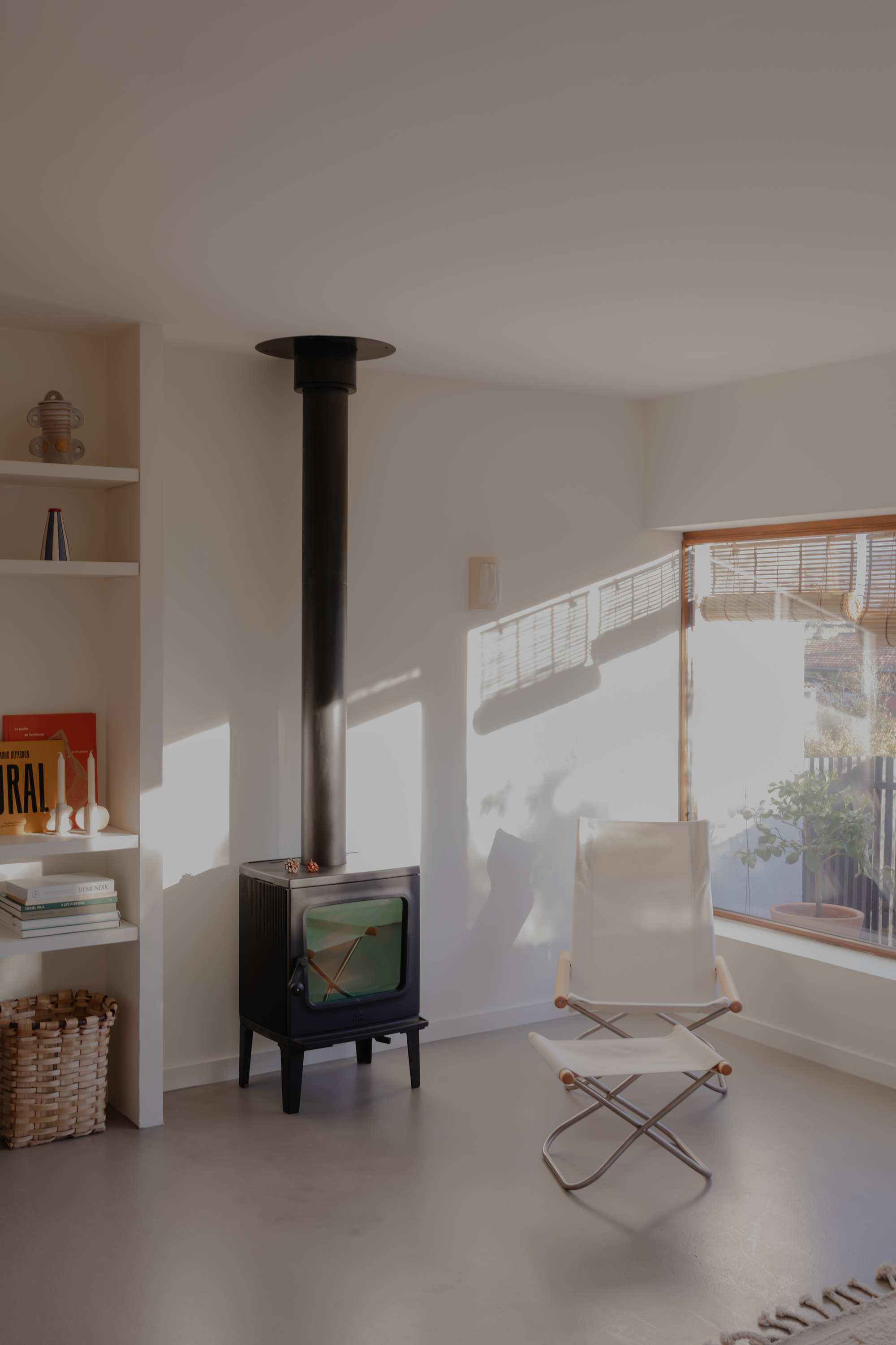 Black freestanding wood stove beside canvas lounge chair with afternoon sun casting window shadows on white walls