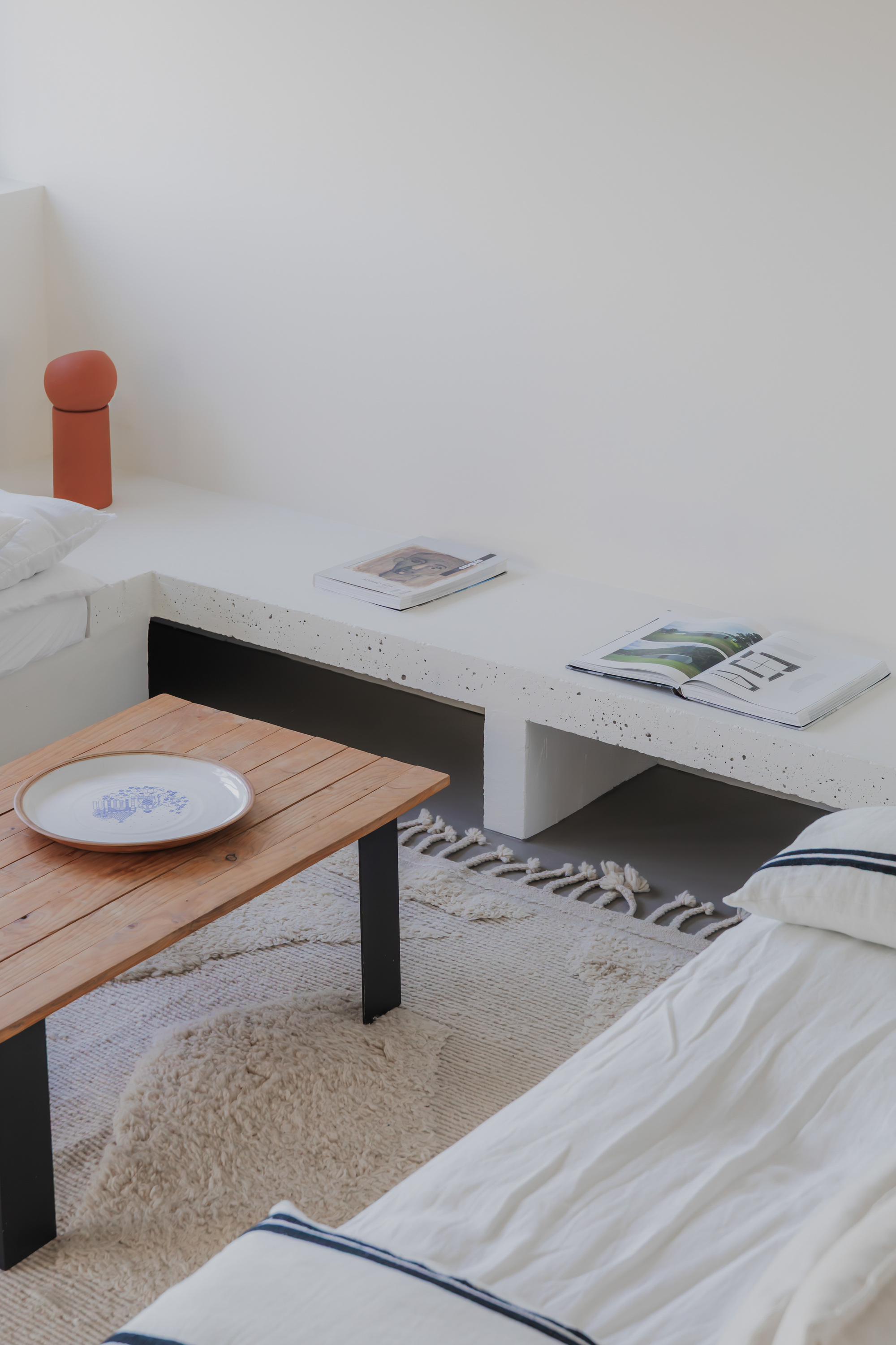 Concrete bench with built-in shelf above timber coffee table and low seating on a jute rug