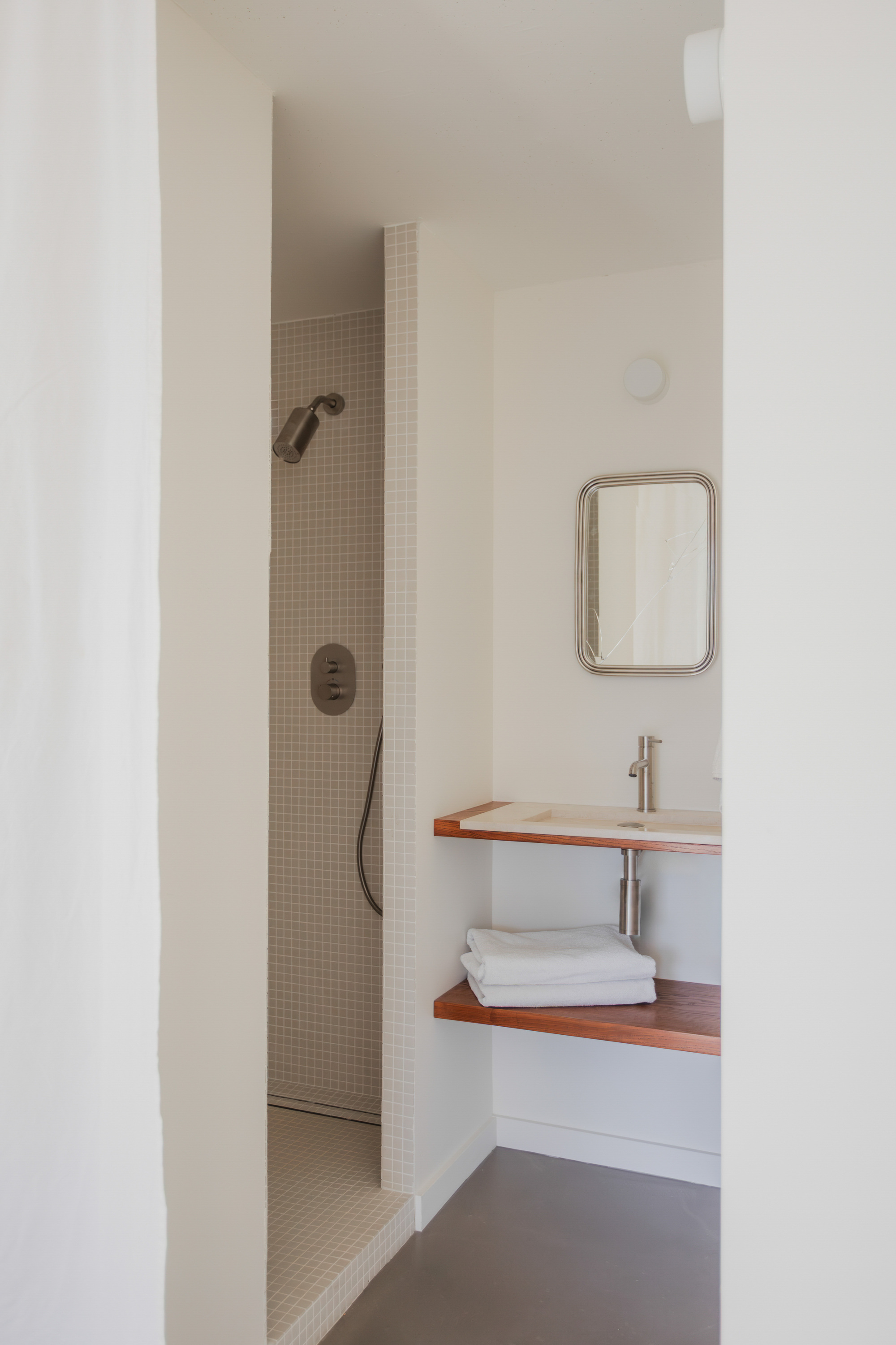 Bathroom view showing mosaic-tiled shower alcove and floating timber vanity with towels beneath