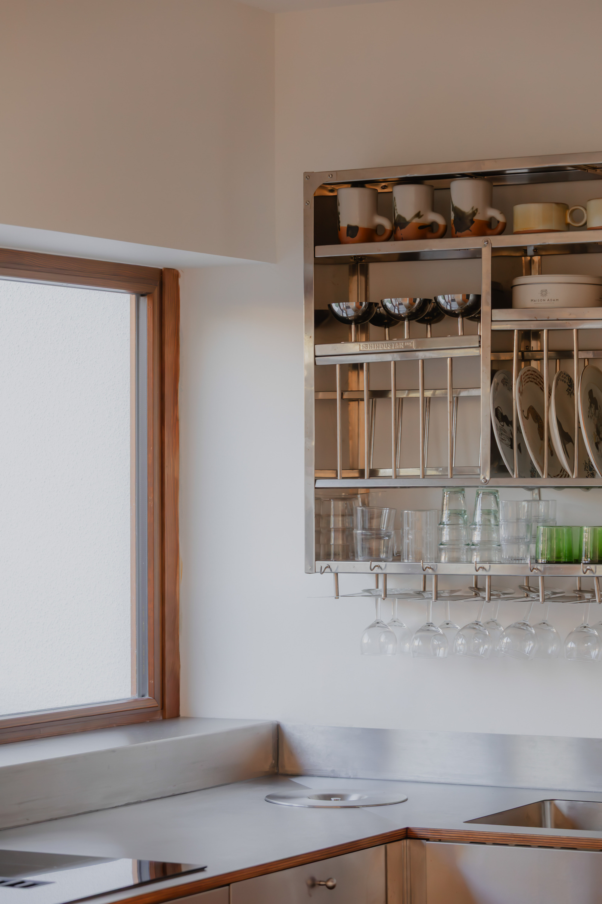 Open kitchen shelving with compartments for cookware, utensils, and glassware beside timber-framed window