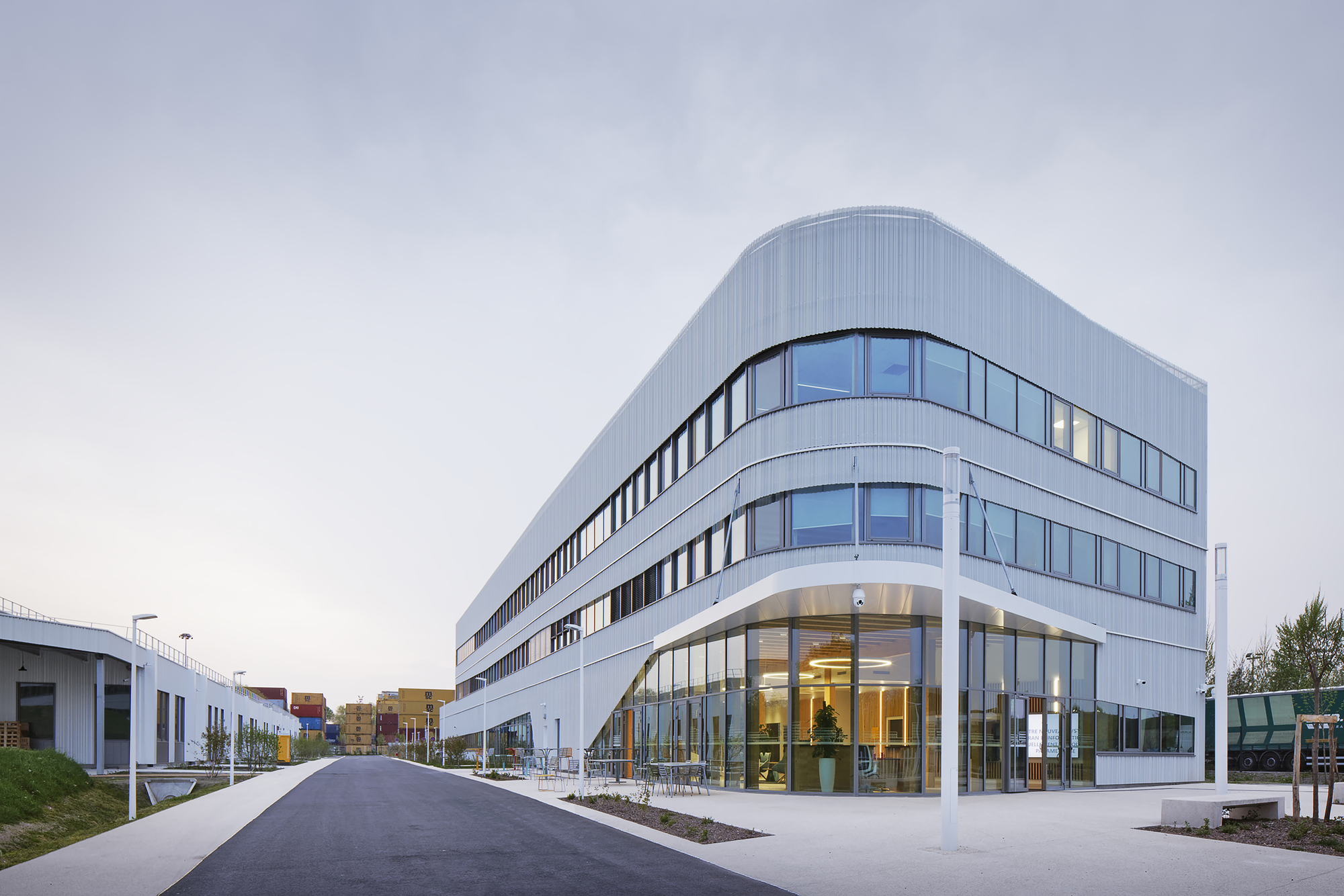 Curved corner entry facade with floor-to-ceiling glass and ribbed metal cladding at dusk