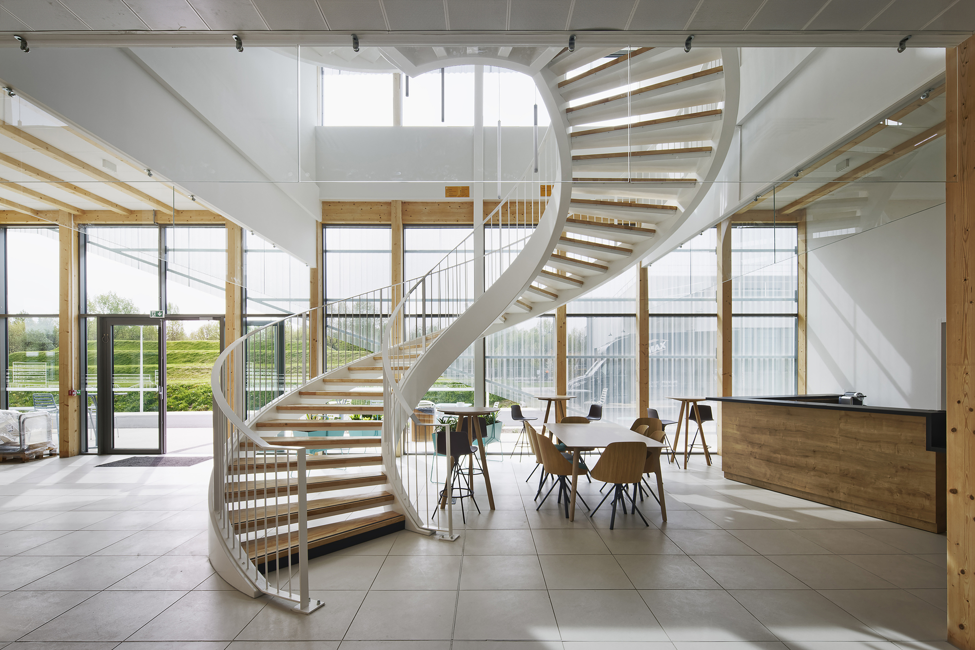 Double-height lobby with a helical staircase in white steel and timber treads under skylights