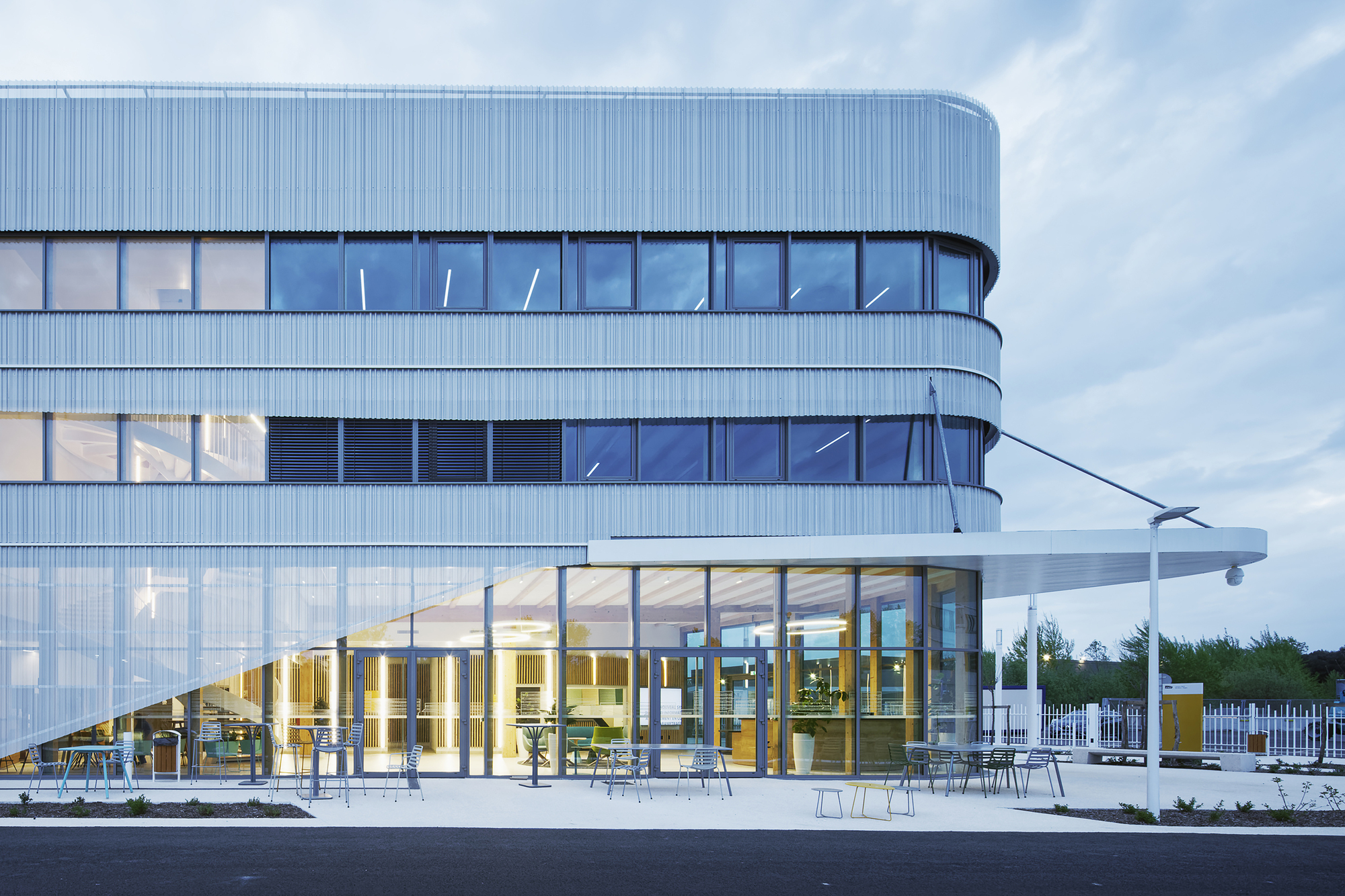 Ground floor terrace with outdoor seating beneath the curved glass facade at twilight