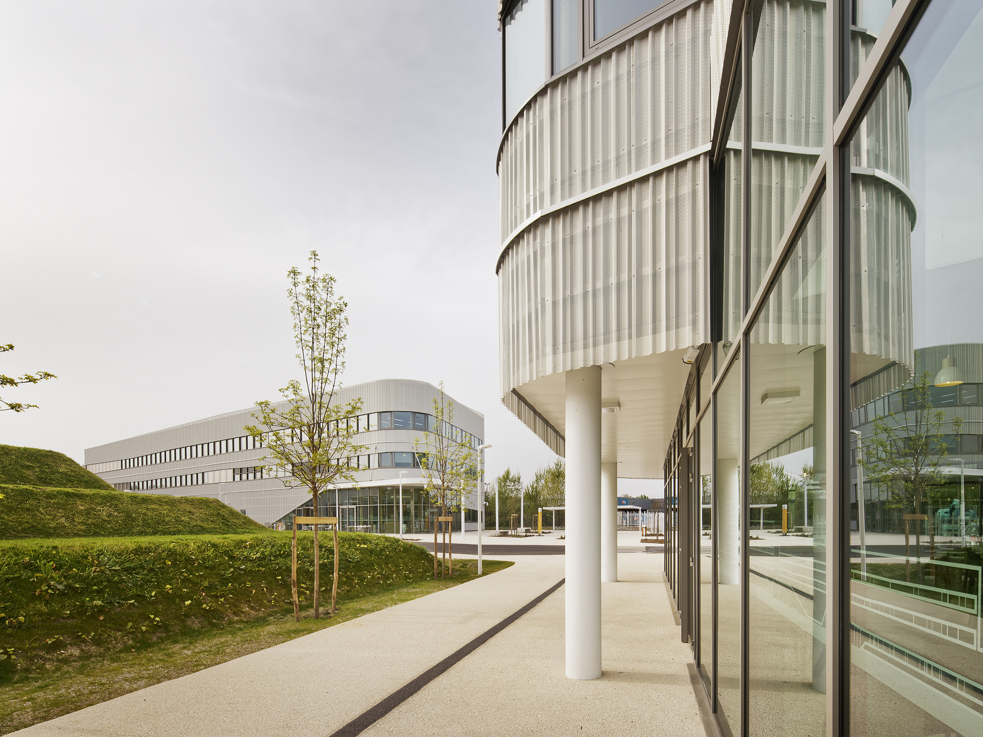 Curved translucent facade with white columns set against a grass berm and young trees