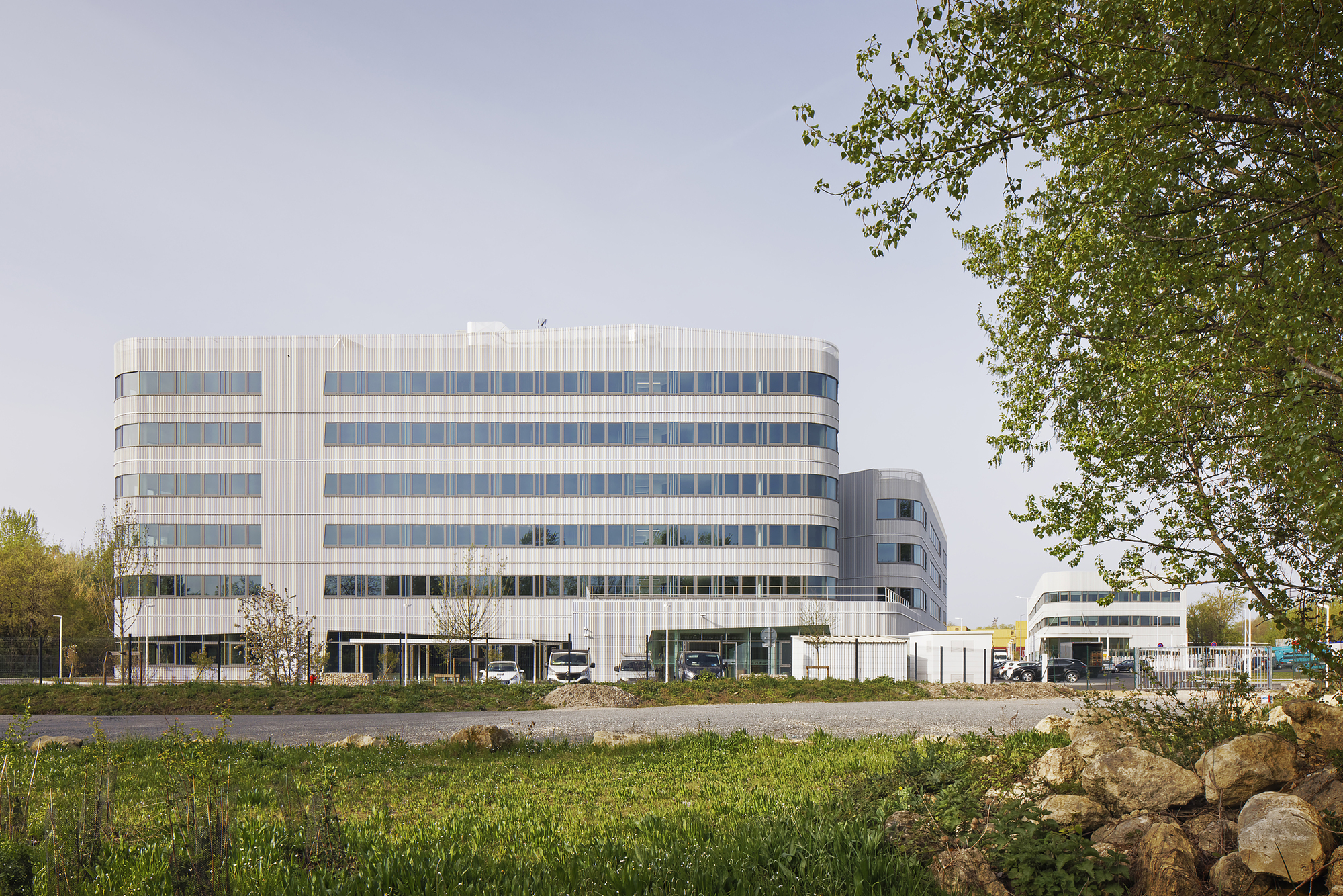 Horizontal striped facade of six-story office building viewed across wild grasses and boulders