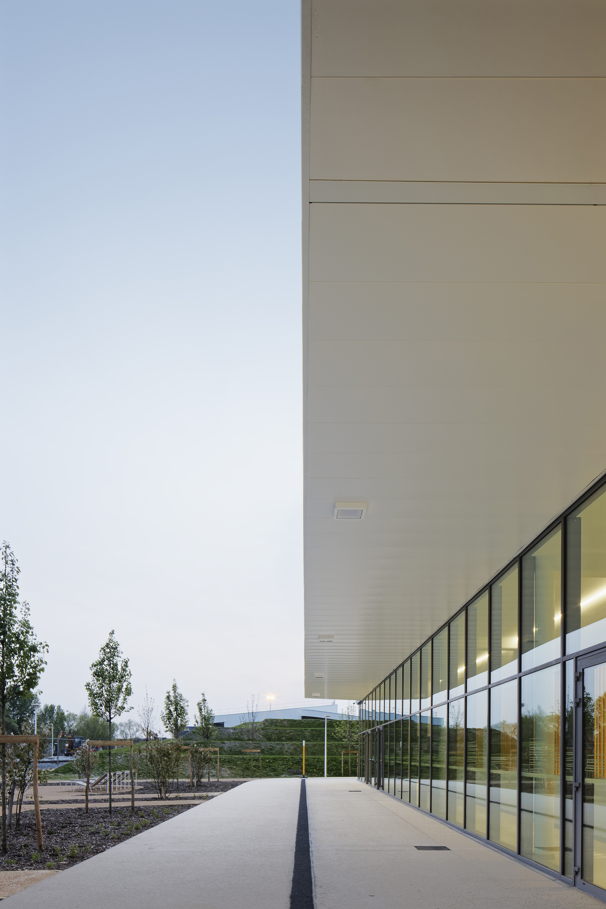 Deep canopy overhang with pale timber soffit extending over a glass-walled corridor