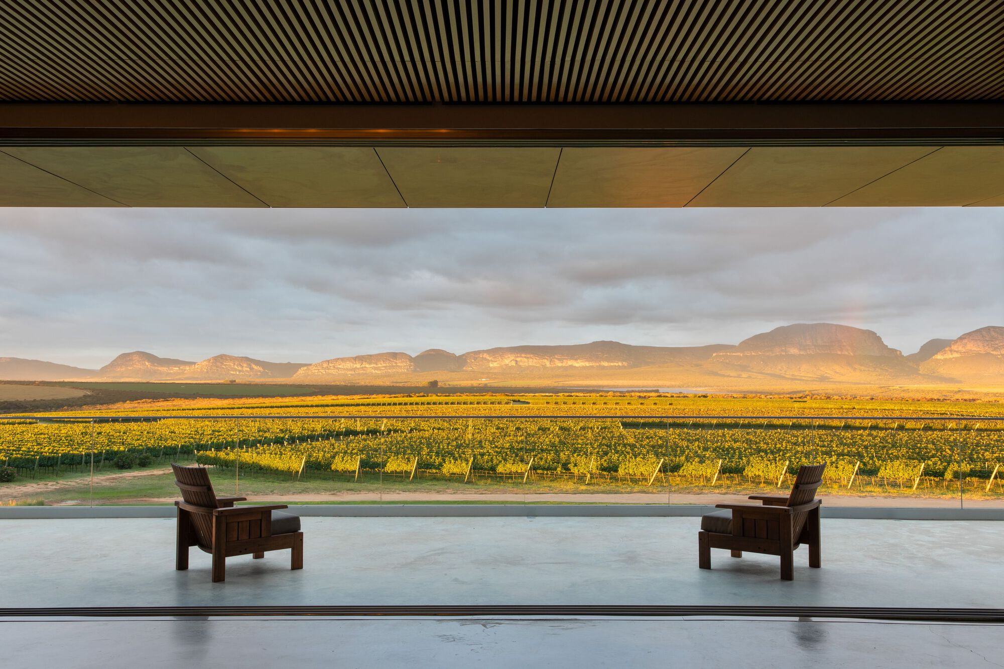 Two timber lounge chairs on a terrace overlooking vineyards bathed in golden afternoon light